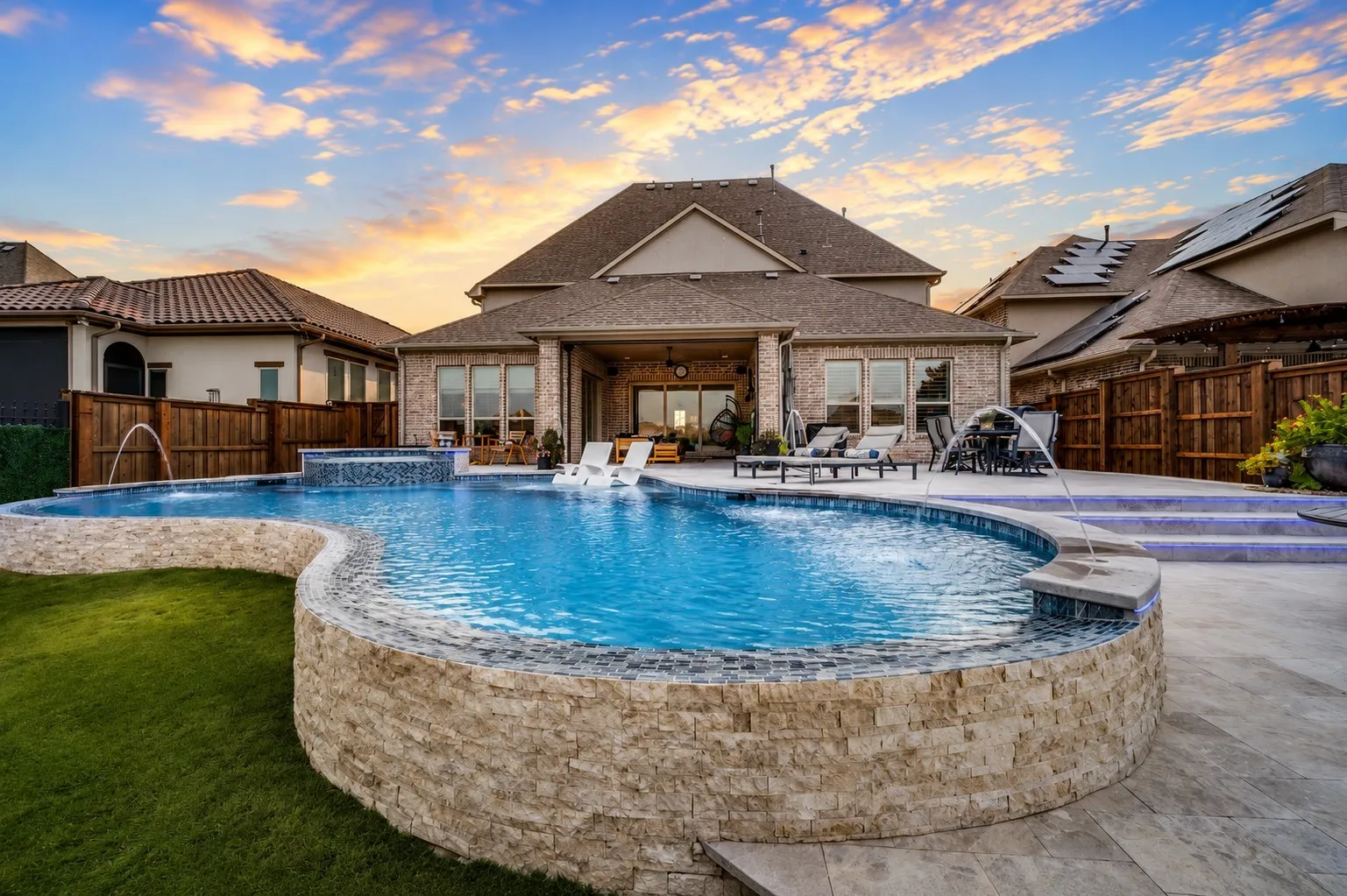 a gorgeous custom pool with elegant stonework, cascading water features, and built-in lounging areas. The expansive patio offers abundant space for relaxing and entertaining, while the covered outdoor living area creates a seamless extension of the home.