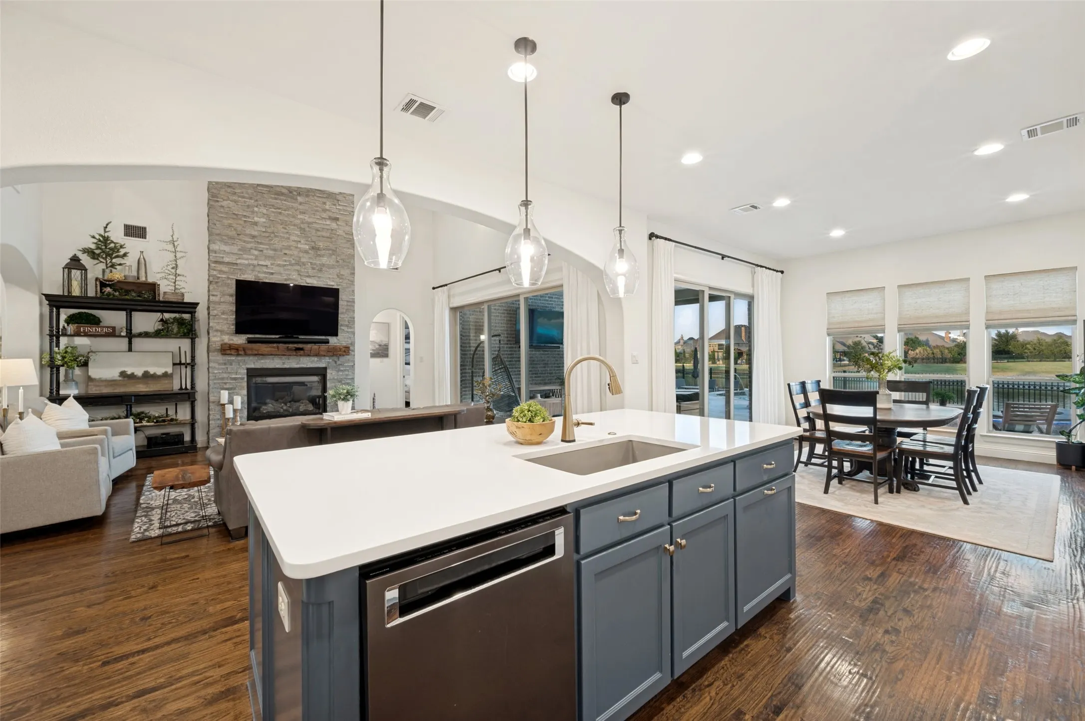 A beautifully designed kitchen centers around a large statement island with sleek quartz countertops, abundant cabinetry, and elegant pendant lighting. The open layout flows effortlessly into the dining and living areas, while expansive windows fill the space with natural light and offer gorgeous views of the backyard and water beyond.