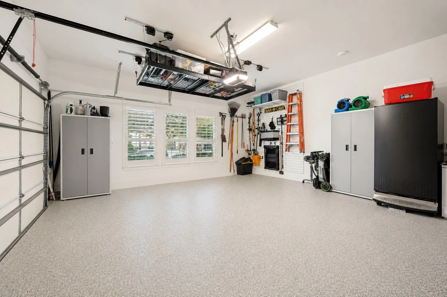This meticulously finished garage combines functionality with thoughtful upgrades, including durable epoxy flooring, an automatic garage lift, and overhead storage to maximize space. Windows with plantation shutters bring in natural light while adding an unexpected touch of style, creating a clean, organized space with plenty of room for vehicles, tools, and storage.