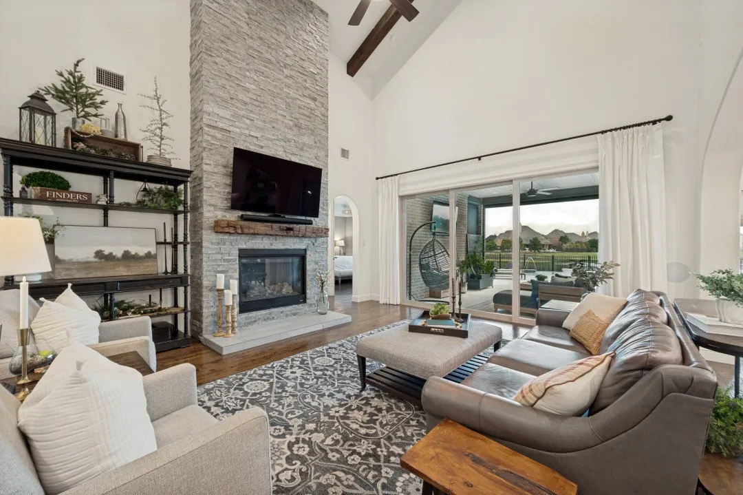 A dramatic floor-to-ceiling stone fireplace anchors this grand living area, complemented by soaring vaulted ceilings. The sliding glass doors bring in abundant natural light while framing beautiful views of the covered patio, pool, and water beyond, creating a seamless connection to the outdoor living space.