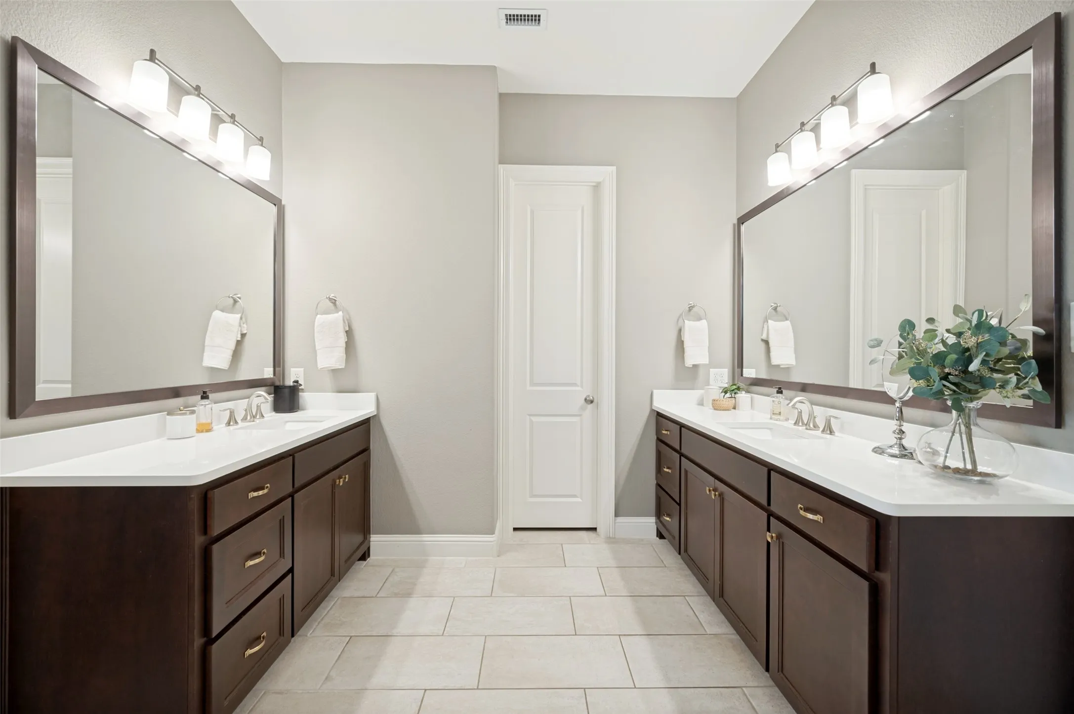 A spacious primary ensuite bath designed with comfort and functionality in mind, featuring separate dual vanities, expansive mirrors, quartz countertops, abundant cabinetry, and elegant finishes. The thoughtful layout provides plenty of personal space and convenient access to the large walk-in closet, creating a beautifully organized and private retreat.