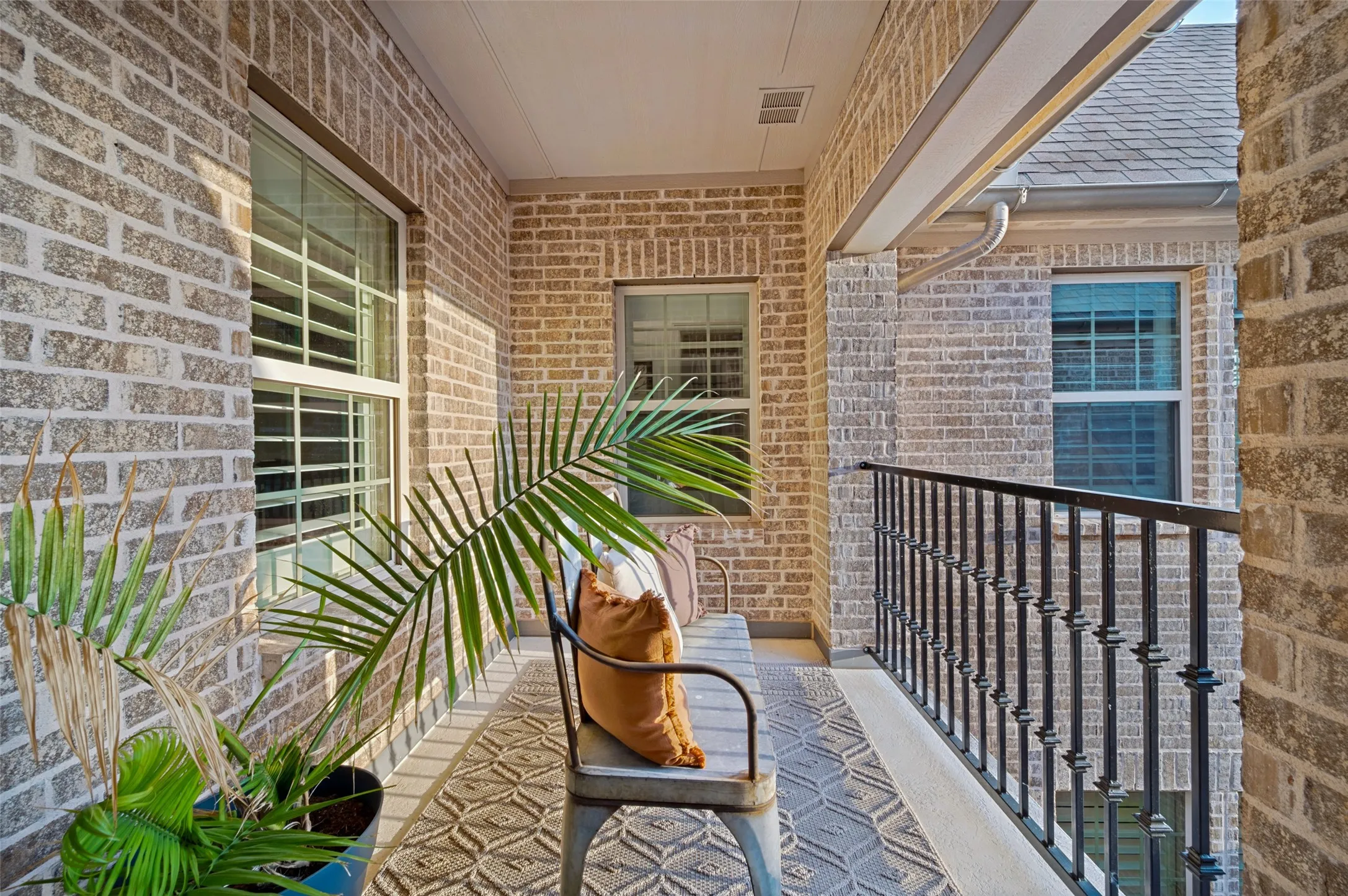 A charming covered terrace overlooking the courtyard entry creates a peaceful outdoor retreat with beautiful architectural views. The brick surround and decorative iron railing add timeless character, while the intimate setting provides the perfect spot to relax and enjoy the fresh air.
