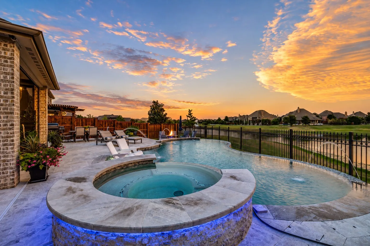 An incredible backyard paradise designed for resort-style living, featuring a sparkling pool and elevated spa enhanced by dramatic accent lighting for a beautiful evening ambiance. The expansive patio offers plenty of room for lounging and entertaining, while the privacy fence creates a secluded retreat.