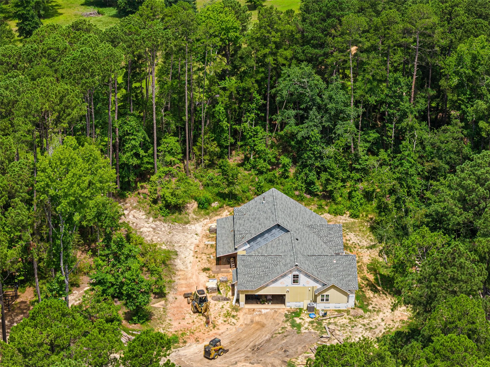 Newly constructed residence with a gray shingle roof and light-colored siding, surrounded by a natural wooded landscape
