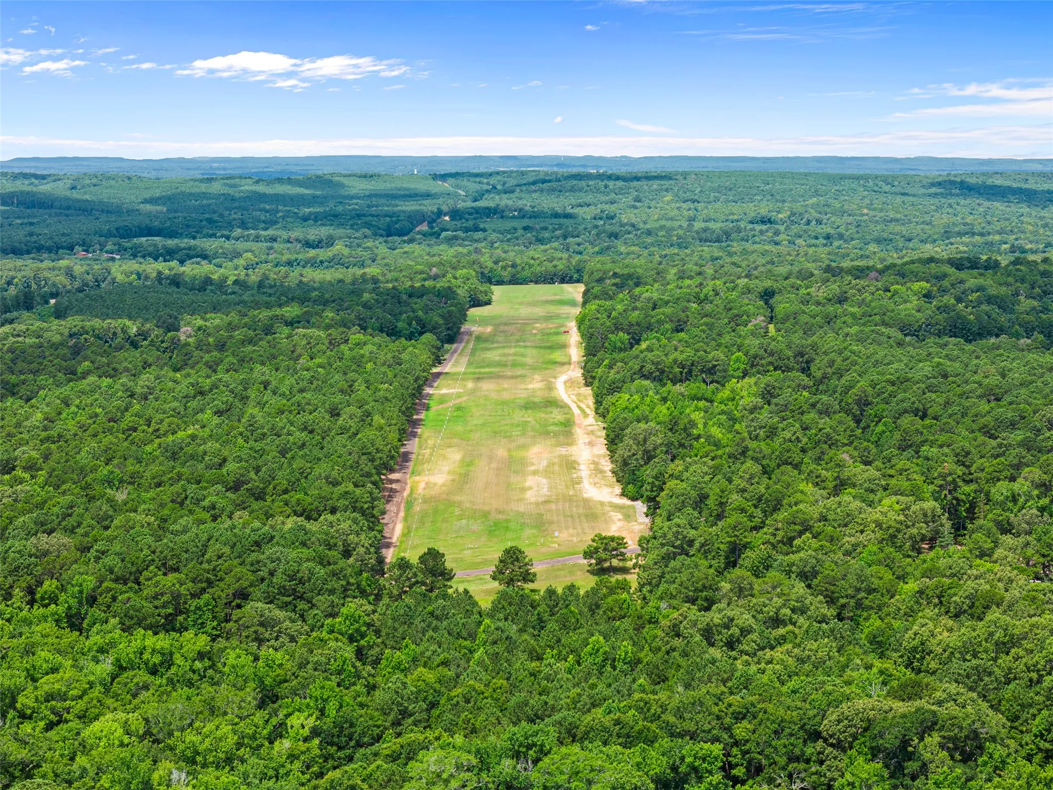 Expansive land parcel featuring cleared acreage bordered by mature trees and a distant tree line