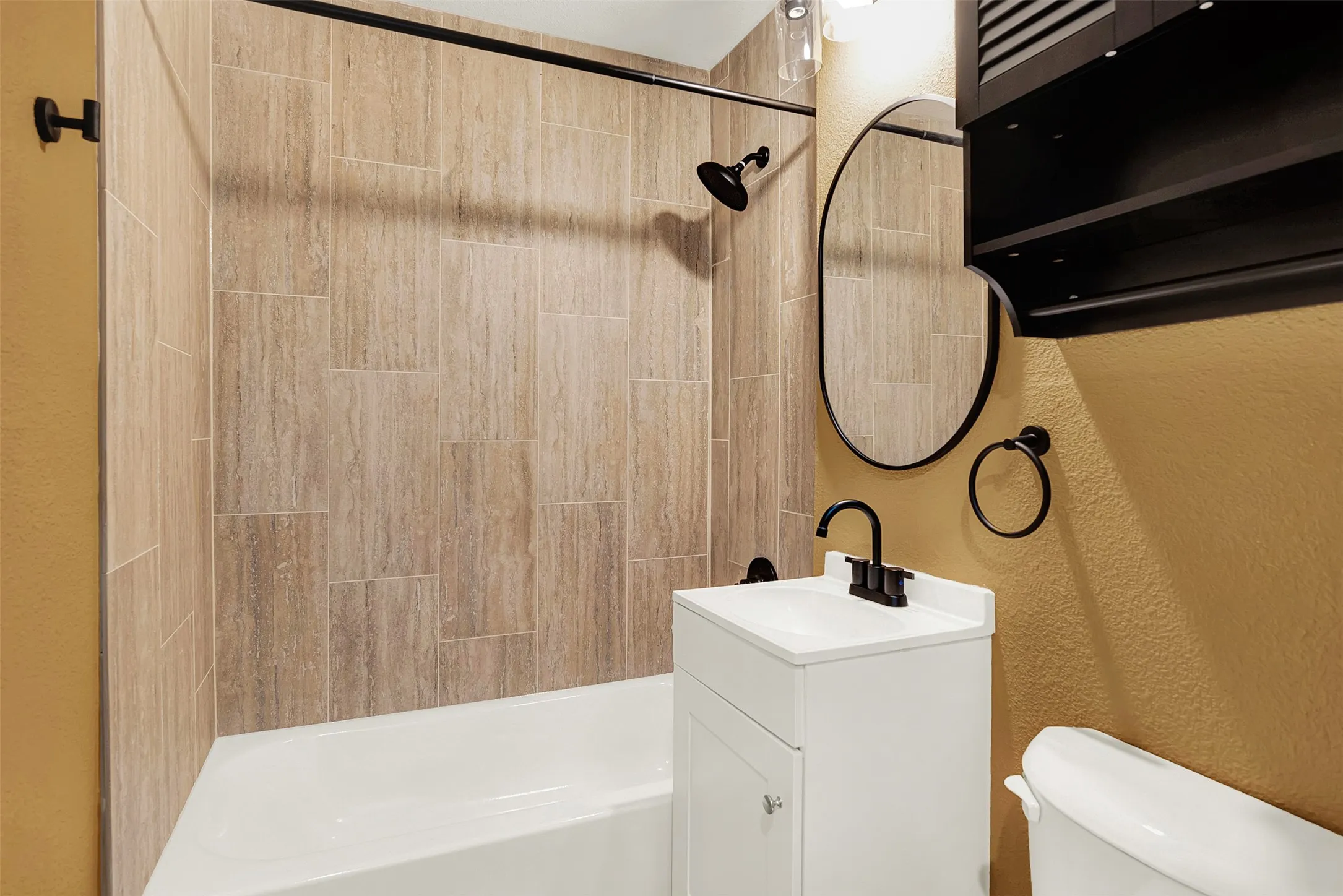 Bathroom with a textured wall, vanity, and washtub / shower combination