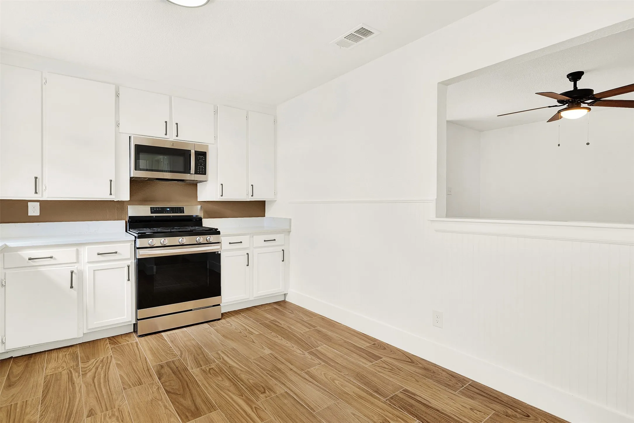 Kitchen featuring appliances with stainless steel finishes, light wood-style floors, light countertops, ceiling fan, and white cabinetry