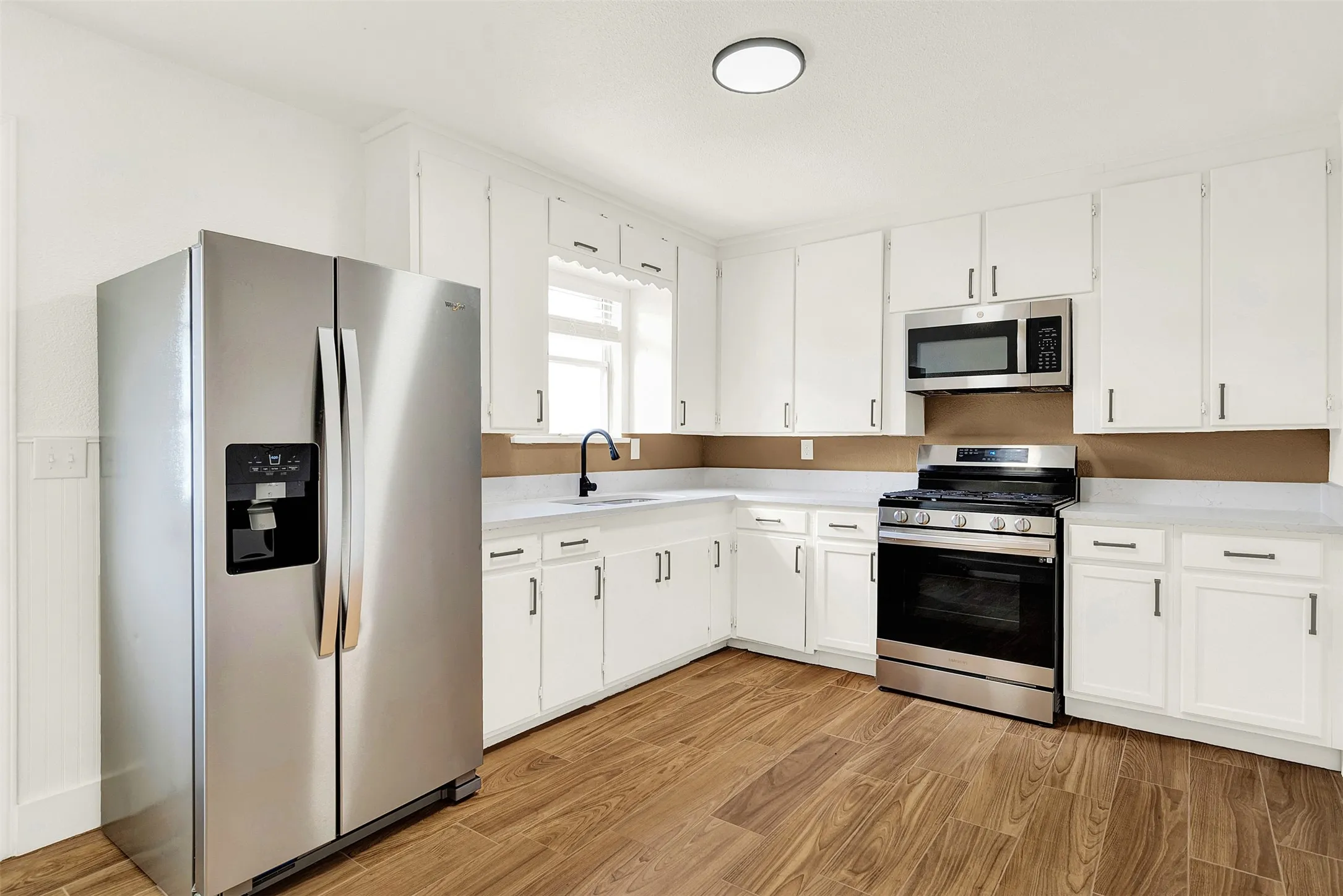 Kitchen featuring stainless steel appliances, light wood-type flooring, light countertops, and white cabinetry