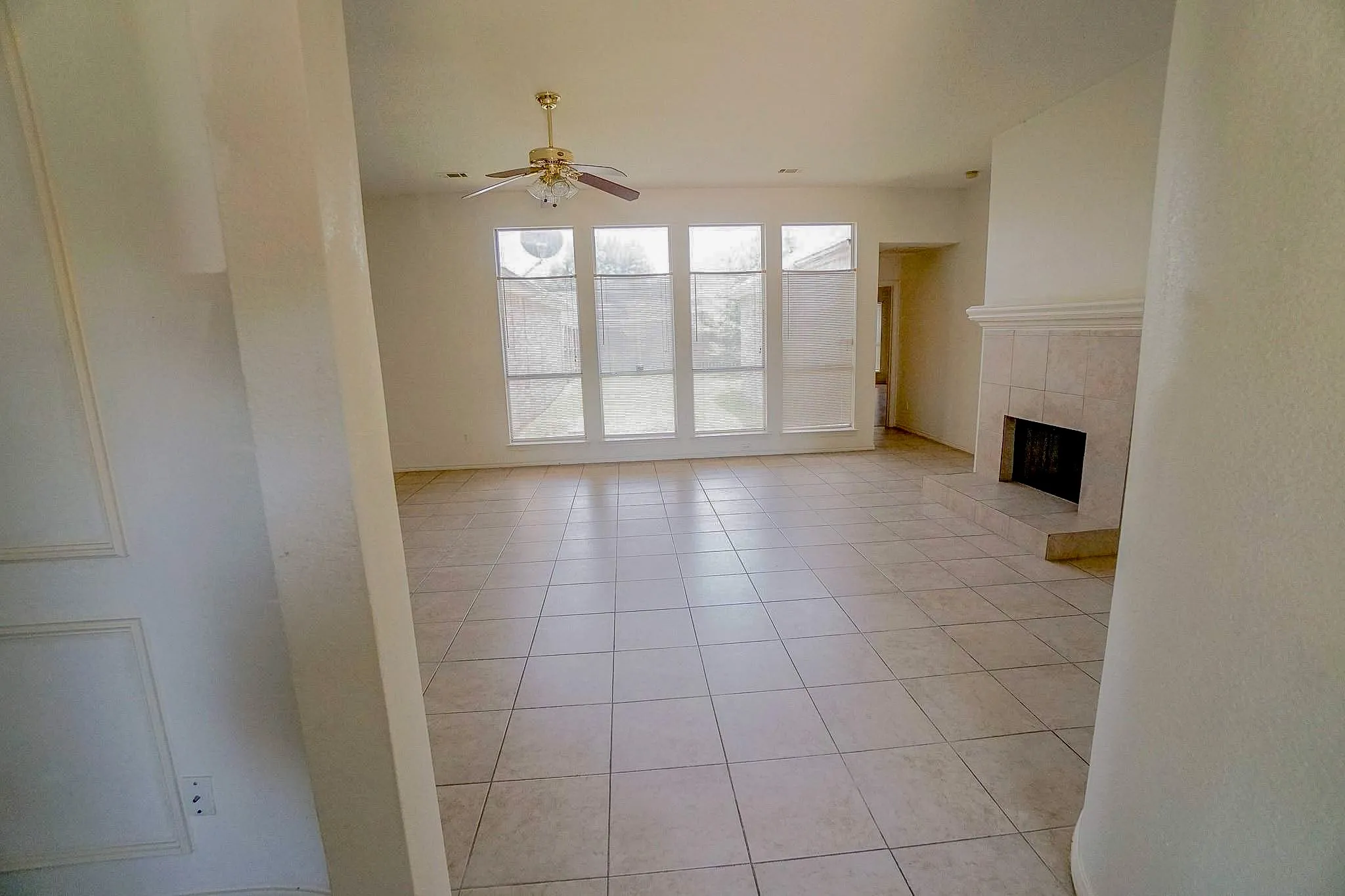 Tiled flooring throughout, a ceiling fan with integrated lighting, a fireplace with a tiled surround, and multiple windows providing natural light