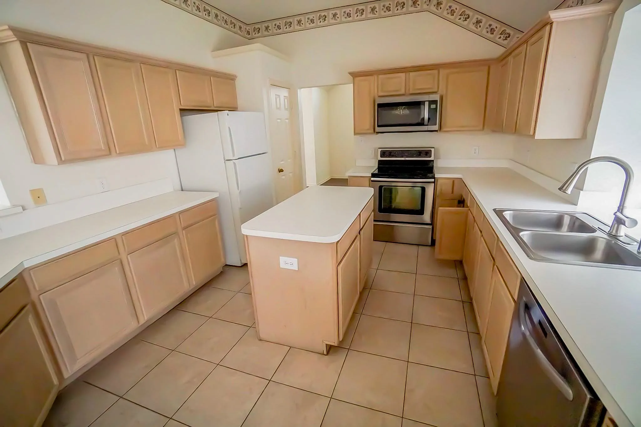 Kitchen featuring a central island, light wood-finish cabinetry, solid surface countertops, a stainless steel double basin sink, and tile flooring