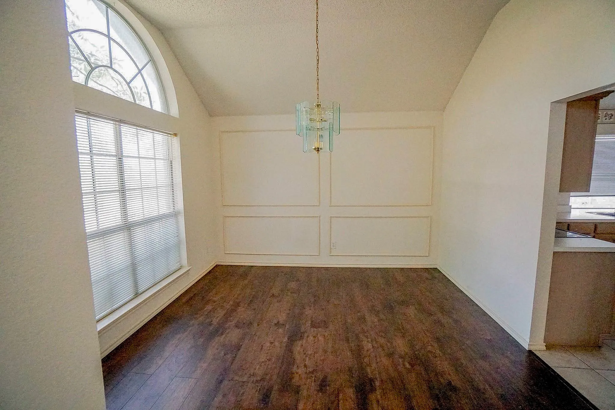 Vaulted ceiling, arched window, wood-finish flooring, decorative wall molding, and a chandelier