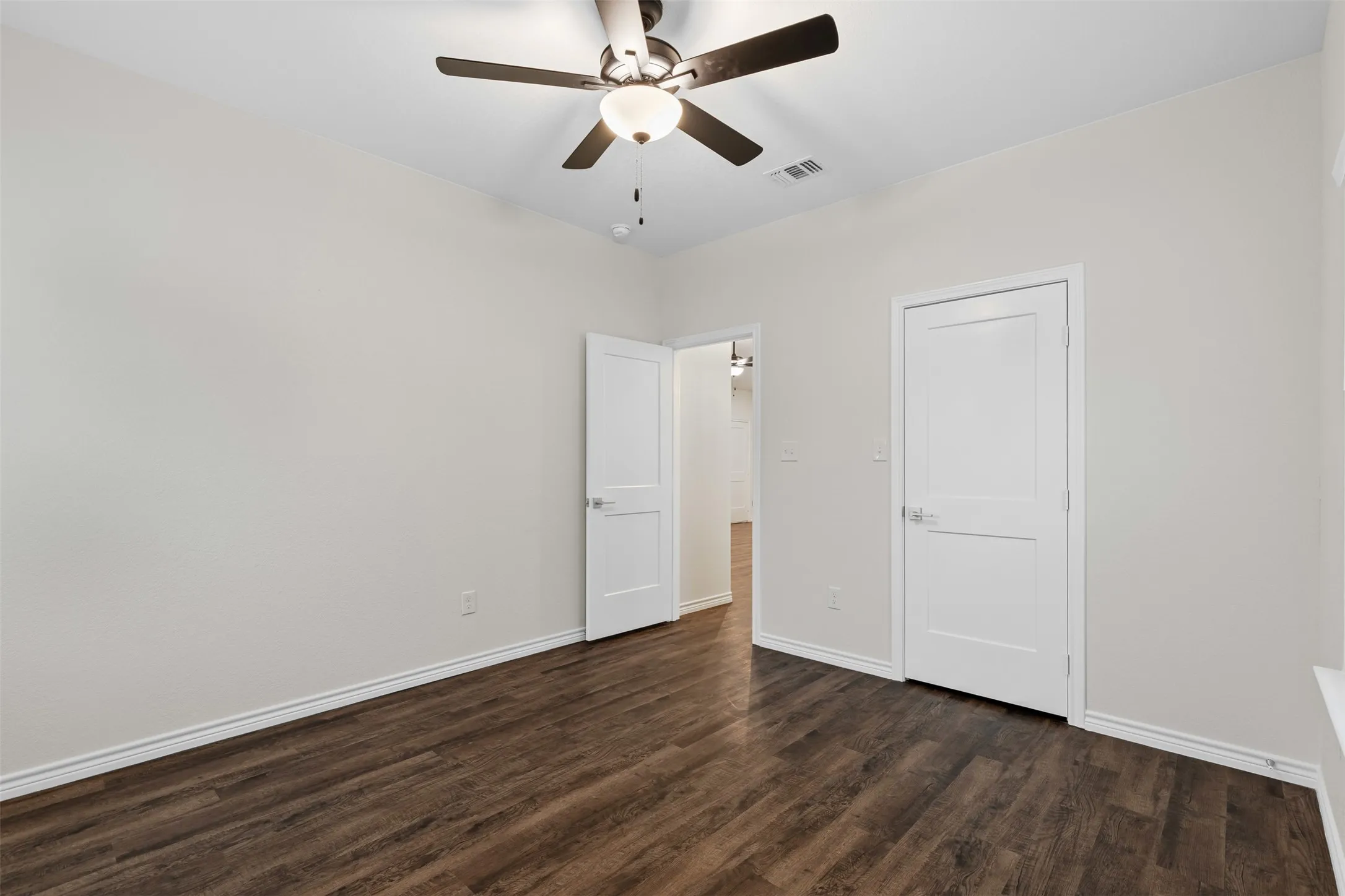 Unfurnished bedroom with dark wood-type flooring, baseboards, and a ceiling fan