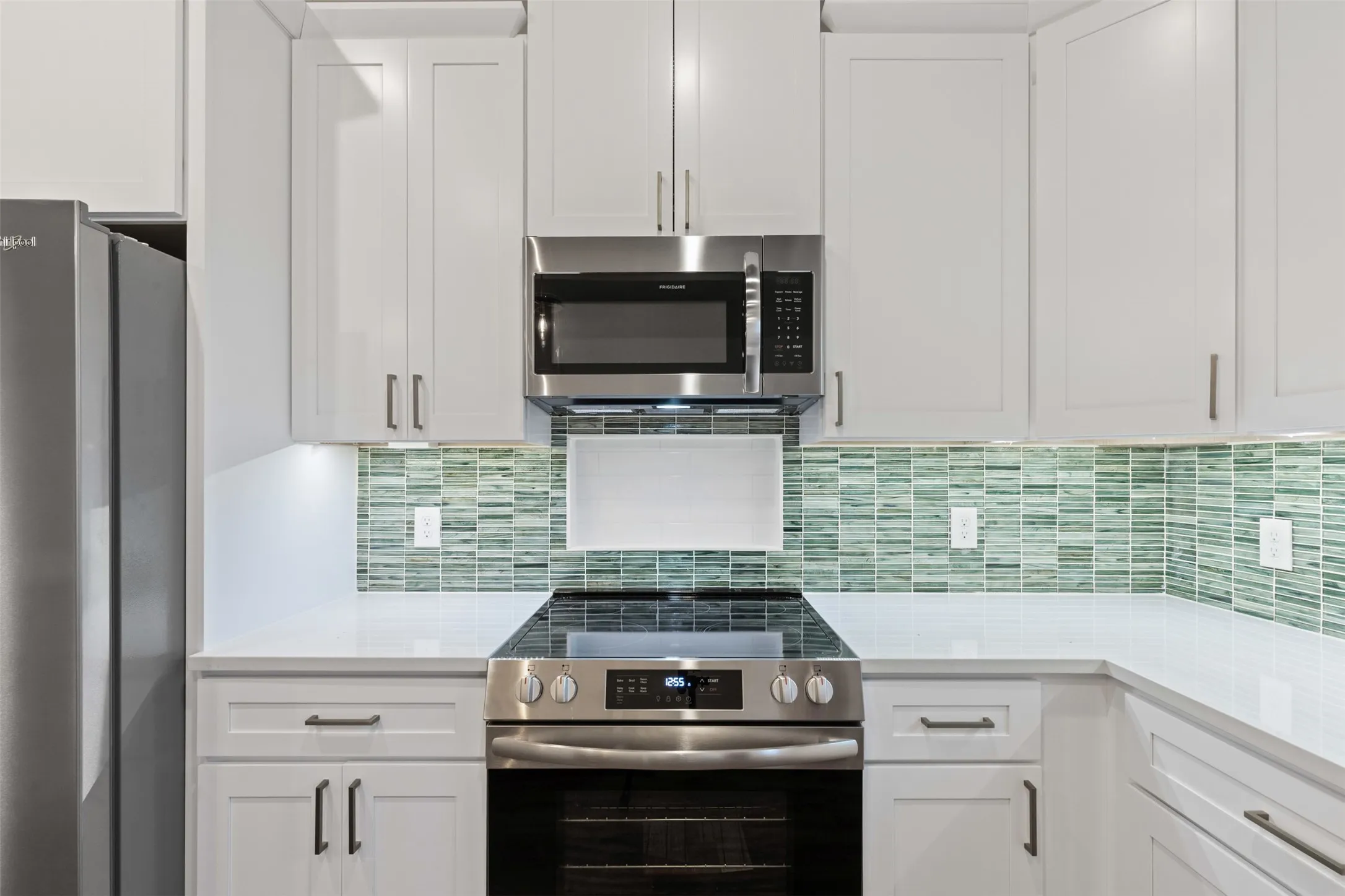 Kitchen featuring stainless steel appliances, white cabinetry, light countertops, and tasteful backsplash