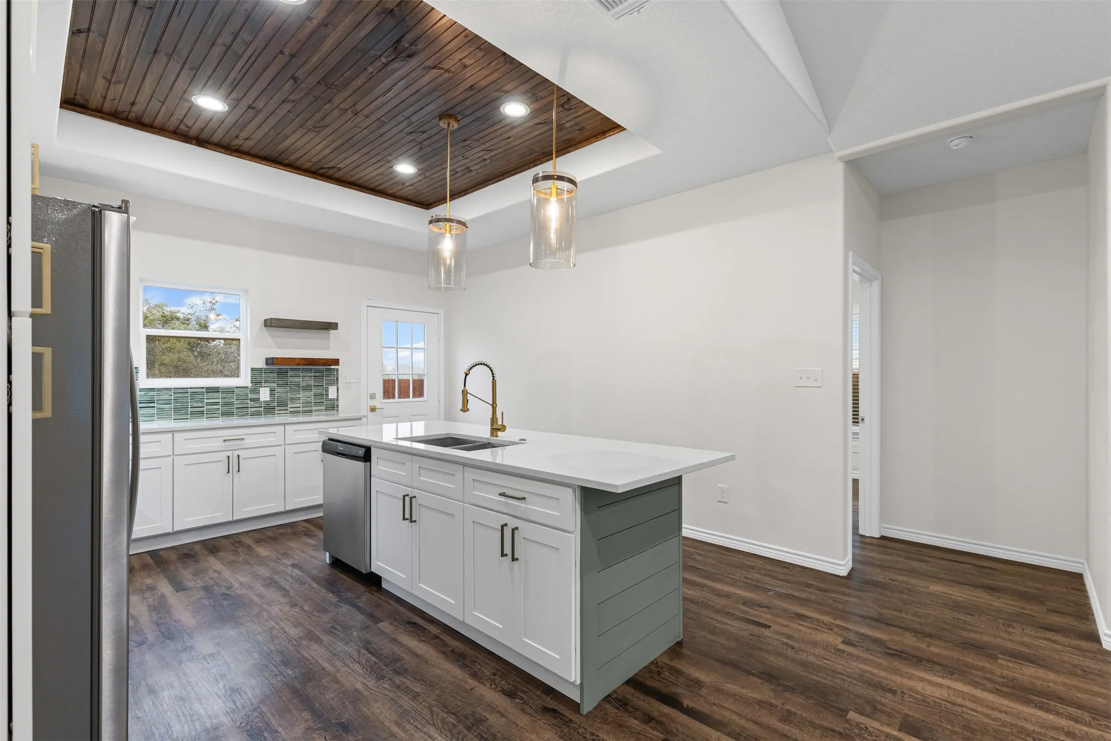 Kitchen featuring stainless steel appliances, a sink, a tray ceiling, dark wood-style floors, and white cabinetry