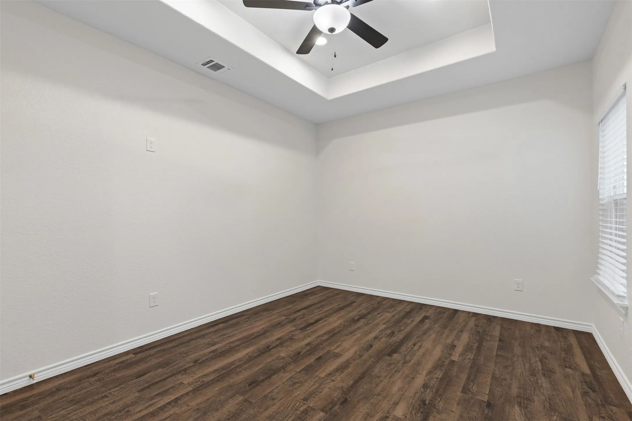 Empty room with dark wood-style flooring, a ceiling fan, a tray ceiling, and baseboards