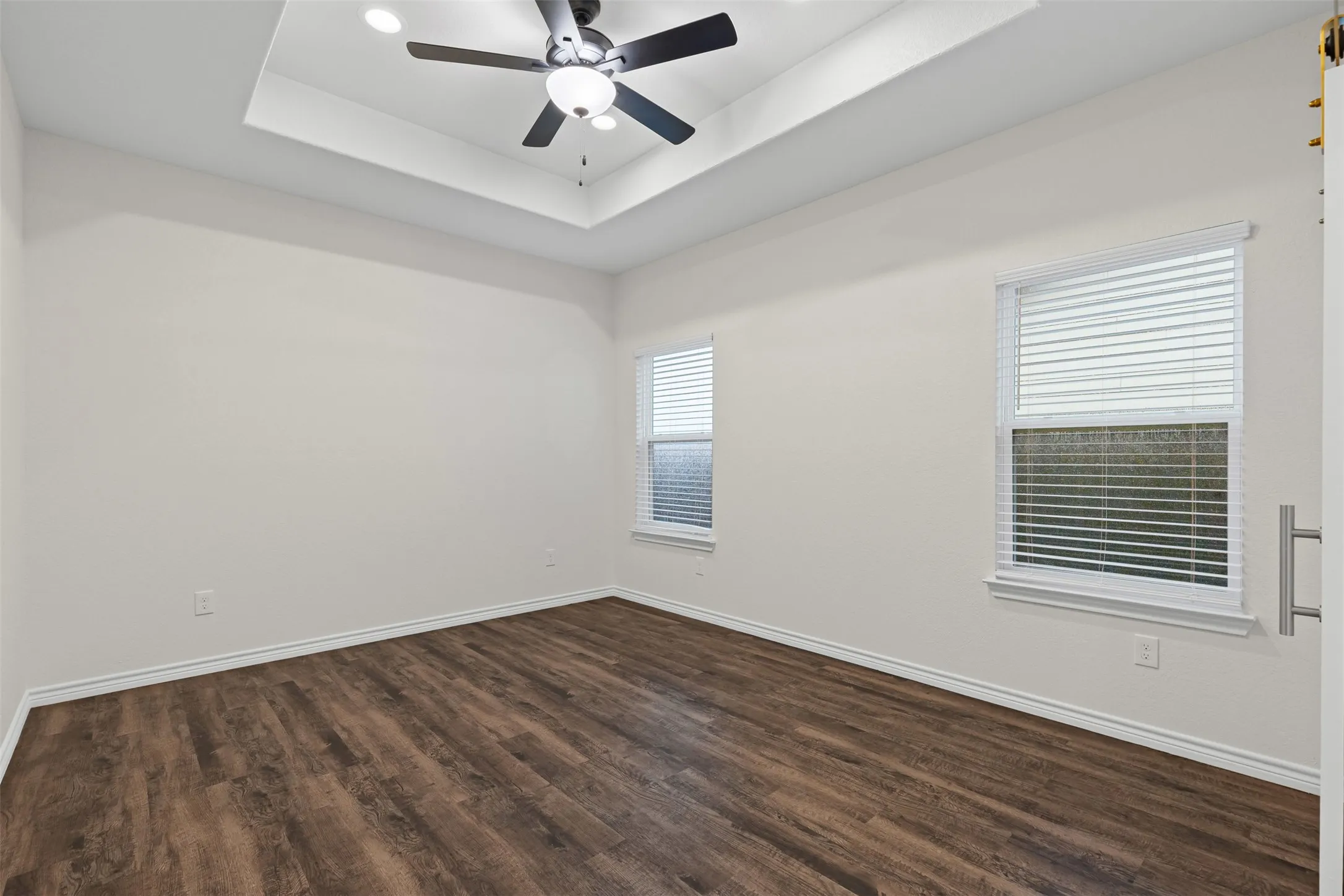 Empty room featuring a raised ceiling, dark wood-style floors, baseboards, and recessed lighting