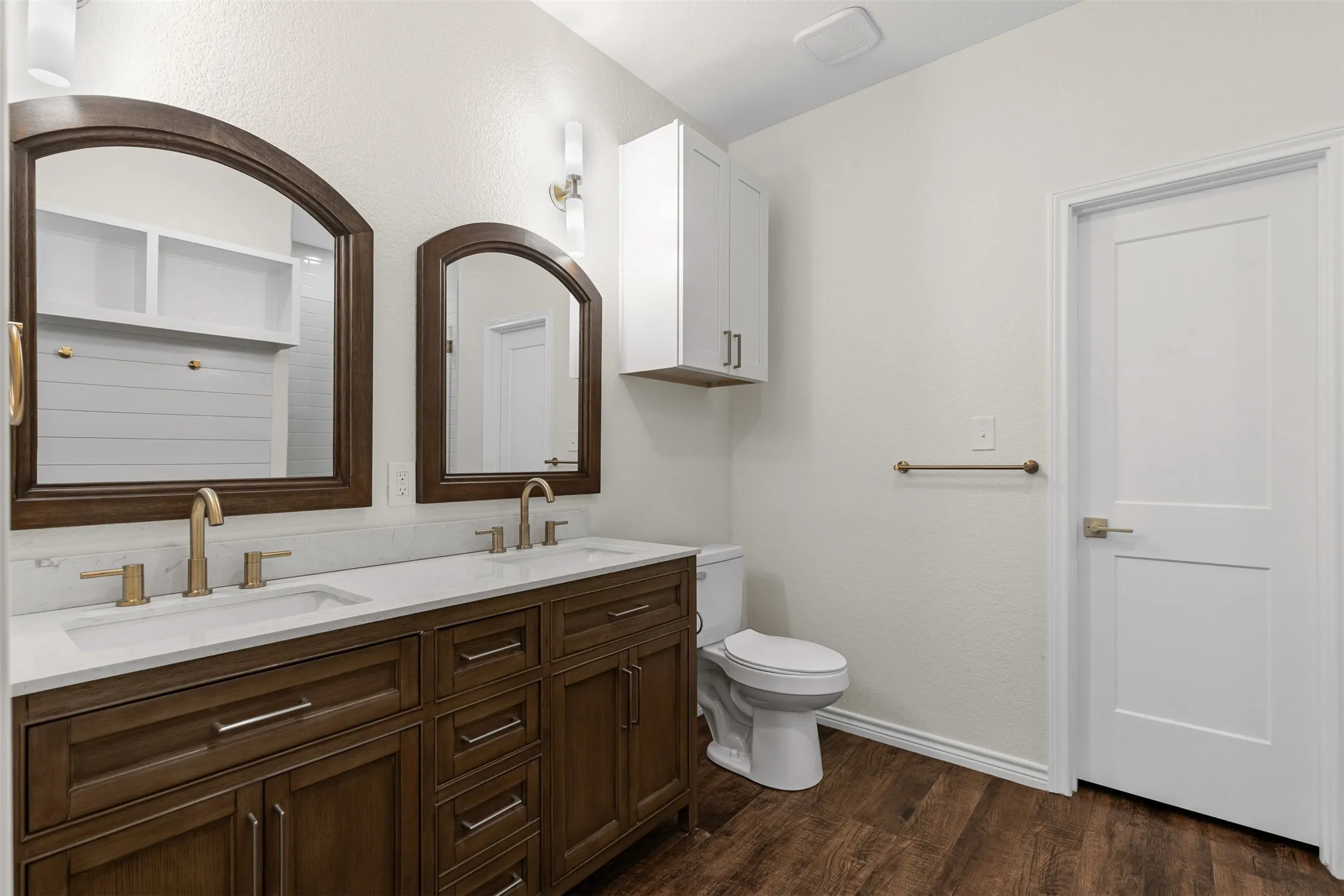 Bathroom featuring double vanity, toilet, wood finished floors, and baseboards
