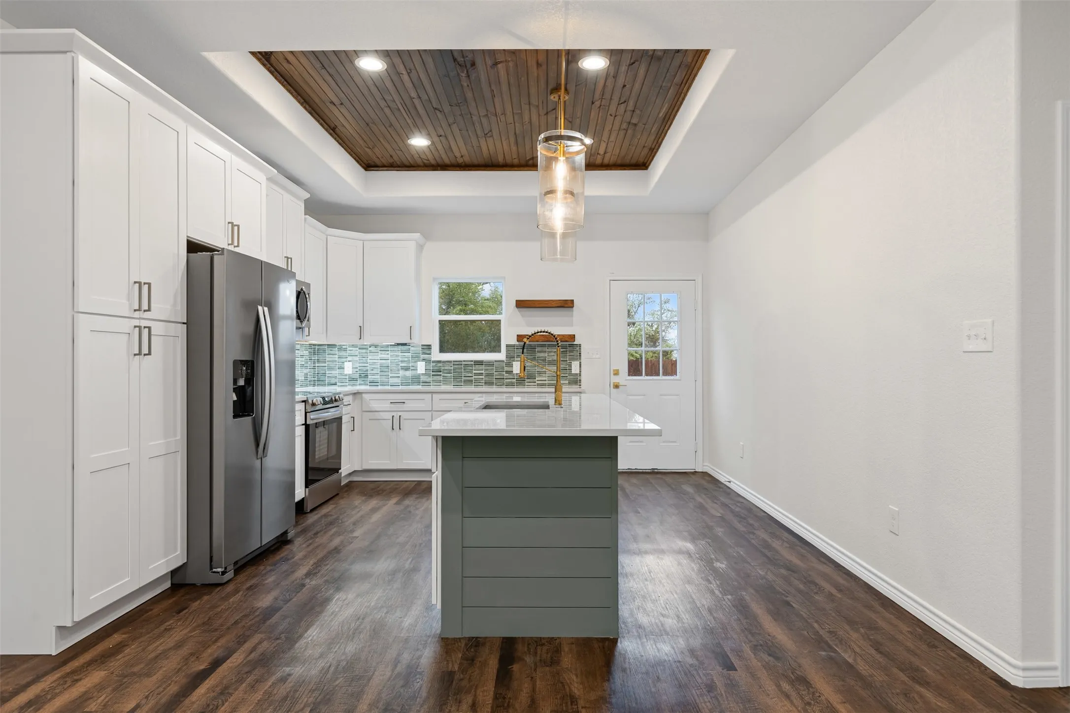 Kitchen featuring a tray ceiling, appliances with stainless steel finishes, a sink, light countertops, and dark wood-type flooring