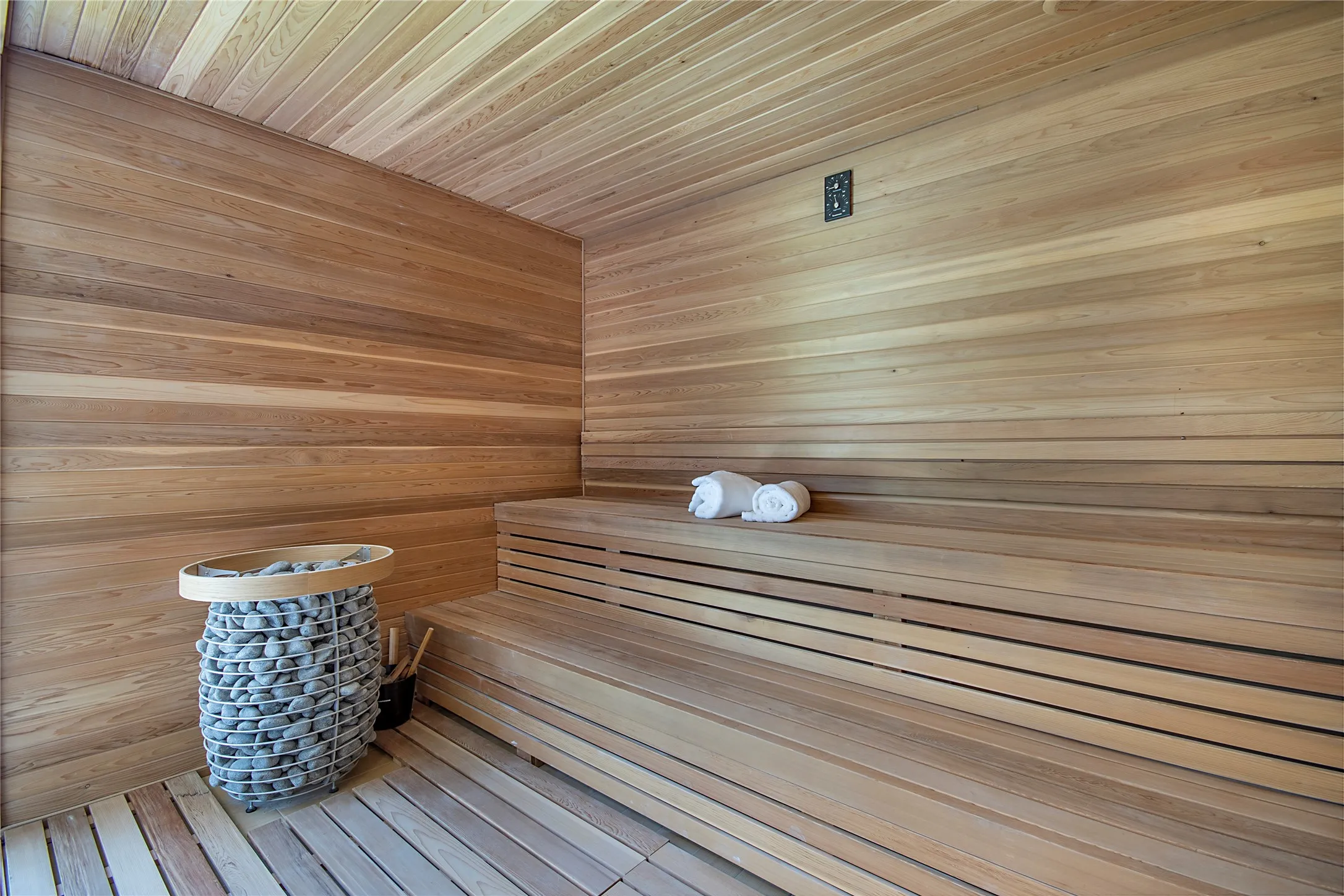 Wood-paneled sauna featuring tiered slatted benches and a stone-filled heating unit