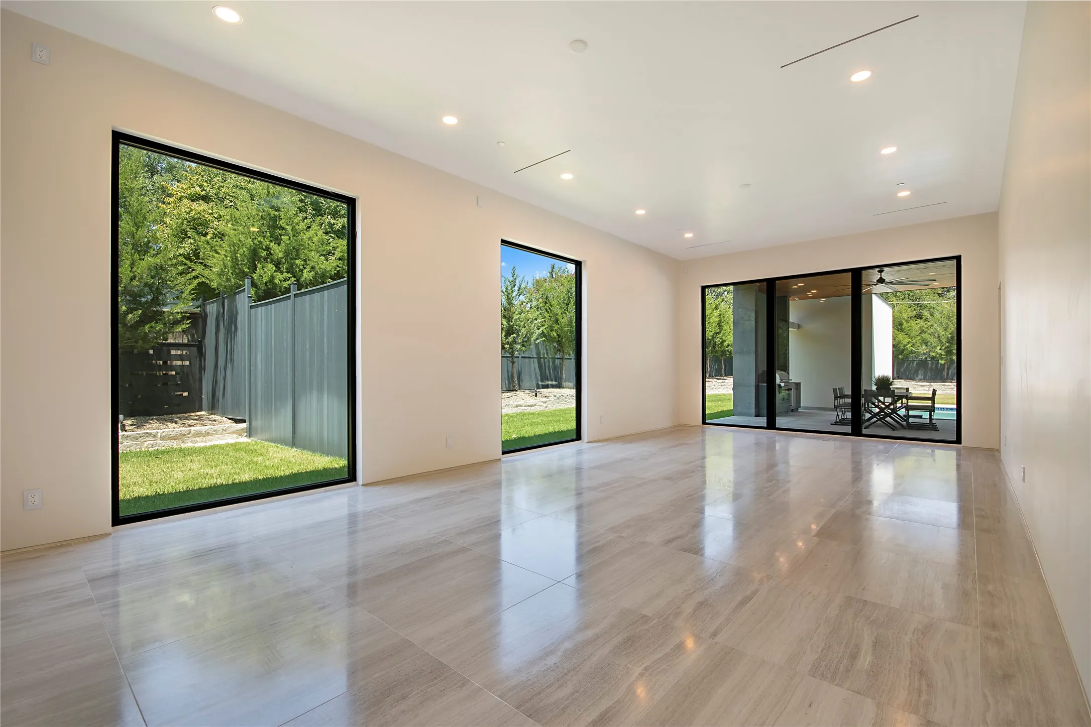 Expansive interior space featuring wide-plank tile flooring, recessed lighting, and a sliding glass door opening to an outdoor patio with a ceiling fan