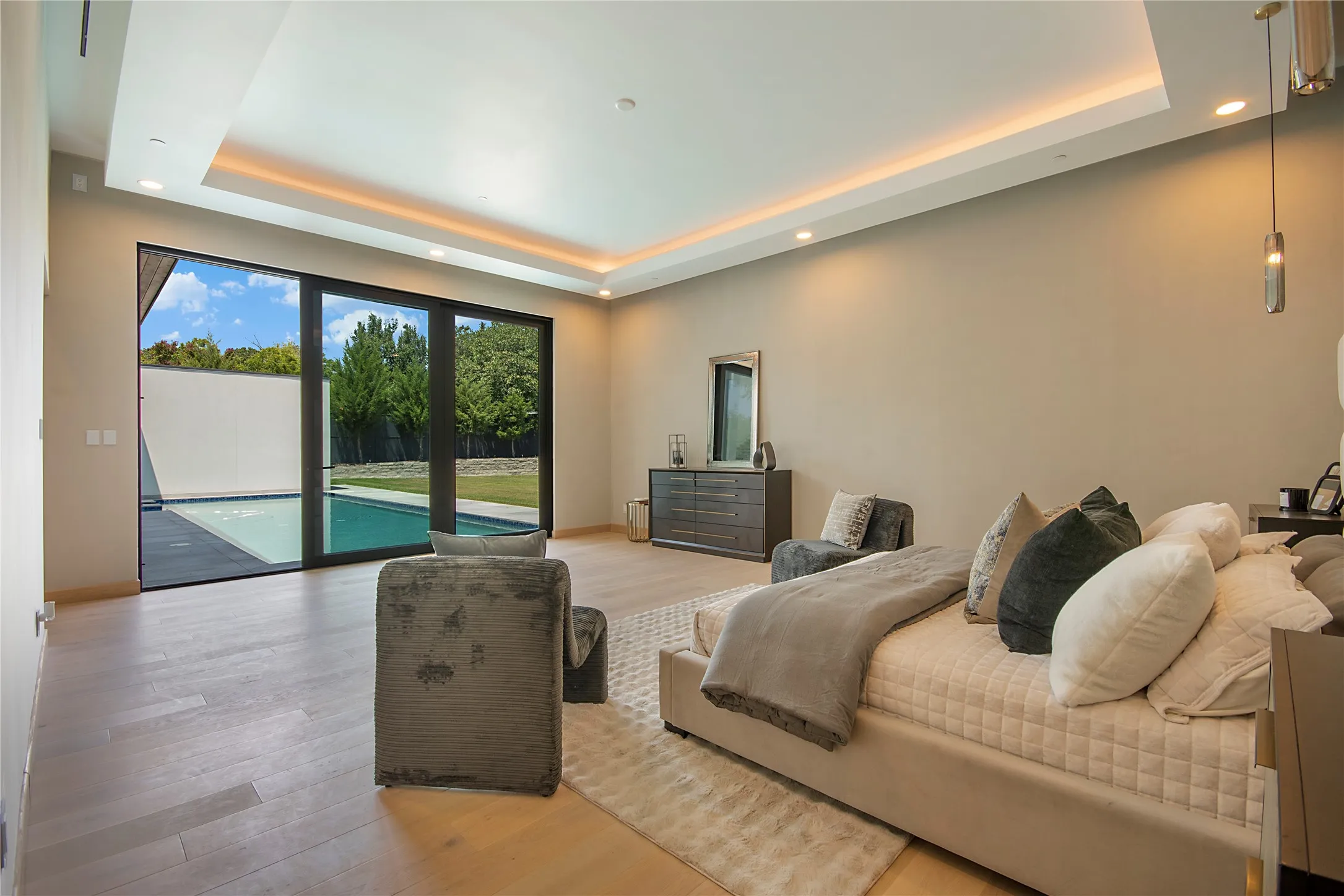 Recessed ceiling lighting, tray ceiling with ambient lighting, wood-finish flooring, full-height sliding glass door, and a private swimming pool