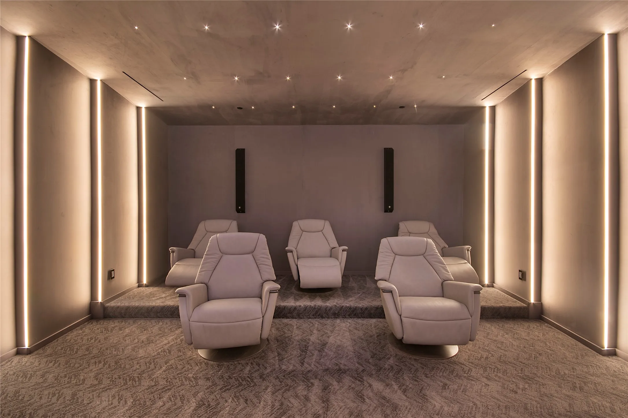 Tiered seating with plush individual chairs, integrated wall lighting, recessed ceiling lights, and patterned carpeting