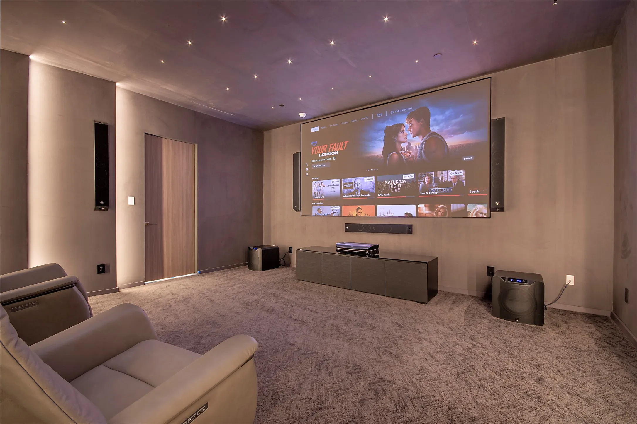 Integrated projection screen with wall-mounted speakers, recessed ceiling lighting, and a neutral-toned carpet