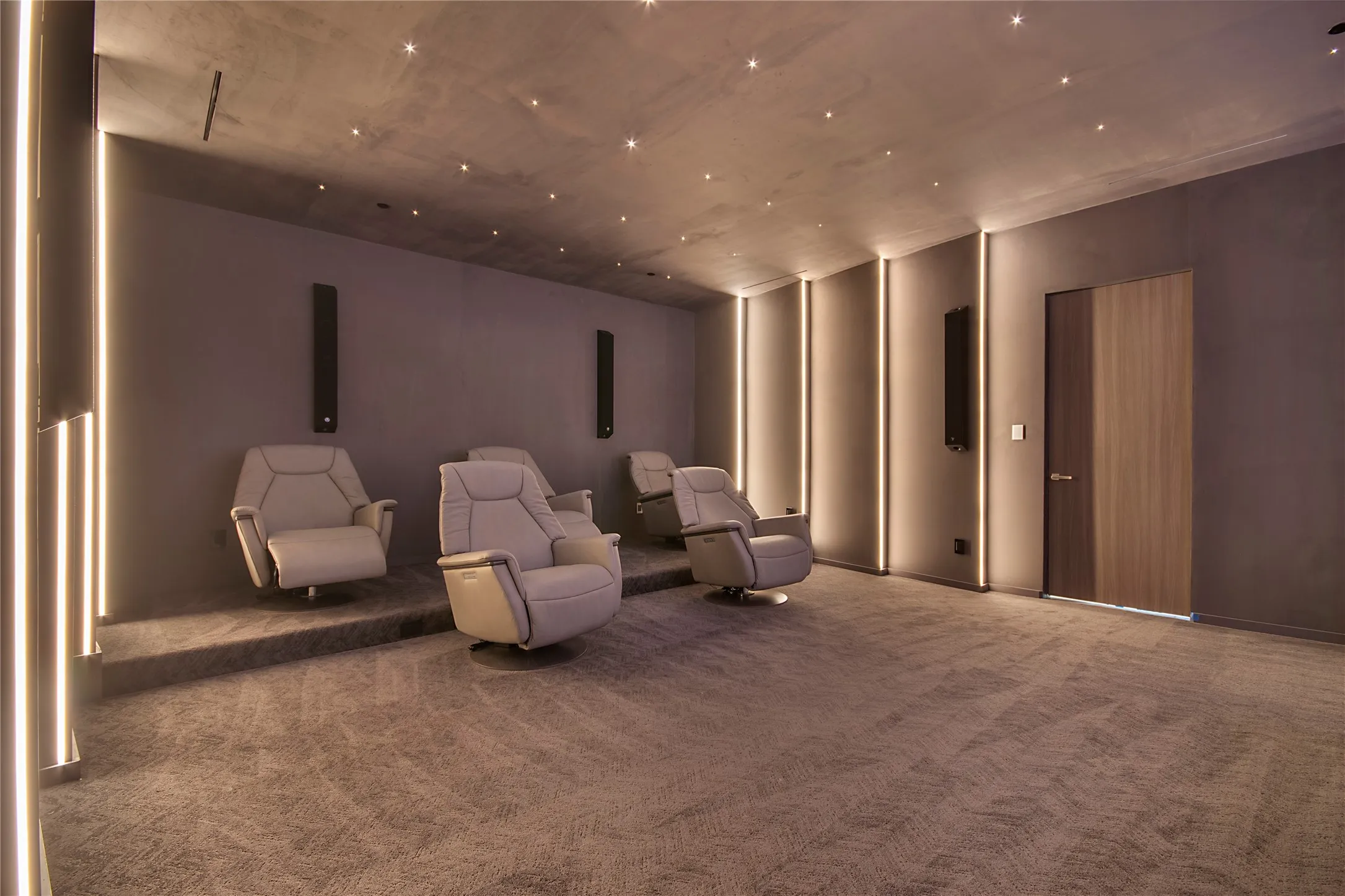 Carpeted media room featuring tiered seating, integrated wall lighting, recessed ceiling lights, and built-in wall speakers