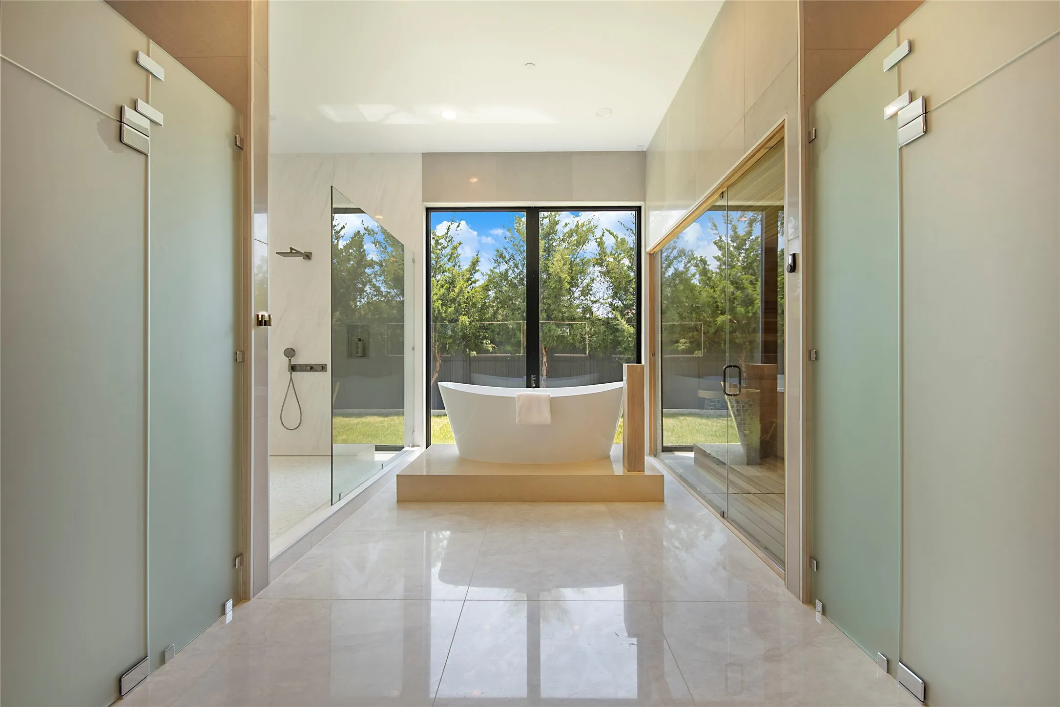 Freestanding soaking tub with a floor-to-ceiling window, glass-enclosed shower, and a built-in sauna