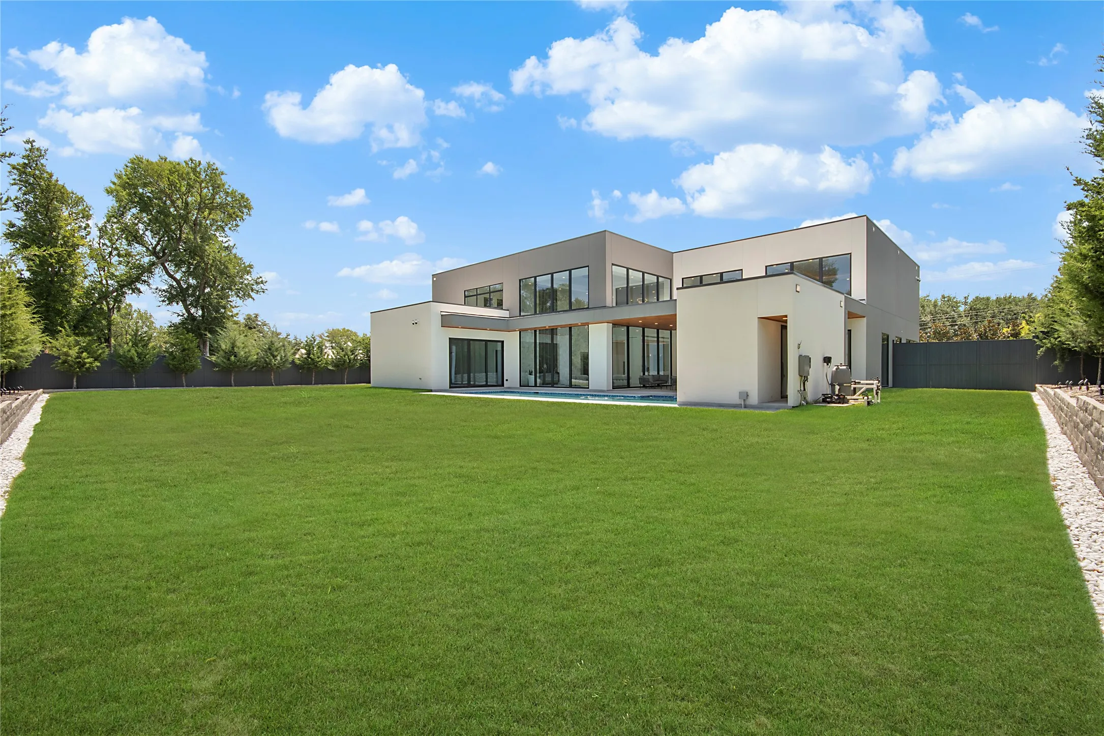 Expansive green lawn bordering a contemporary exterior with multiple large windows, a private pool area, and perimeter landscaping