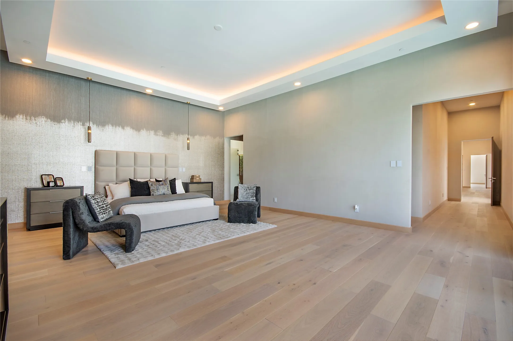 Tray ceiling with recessed lighting and cove lighting, accent wall with textured wallcovering, wood-finish flooring, and a wide entryway