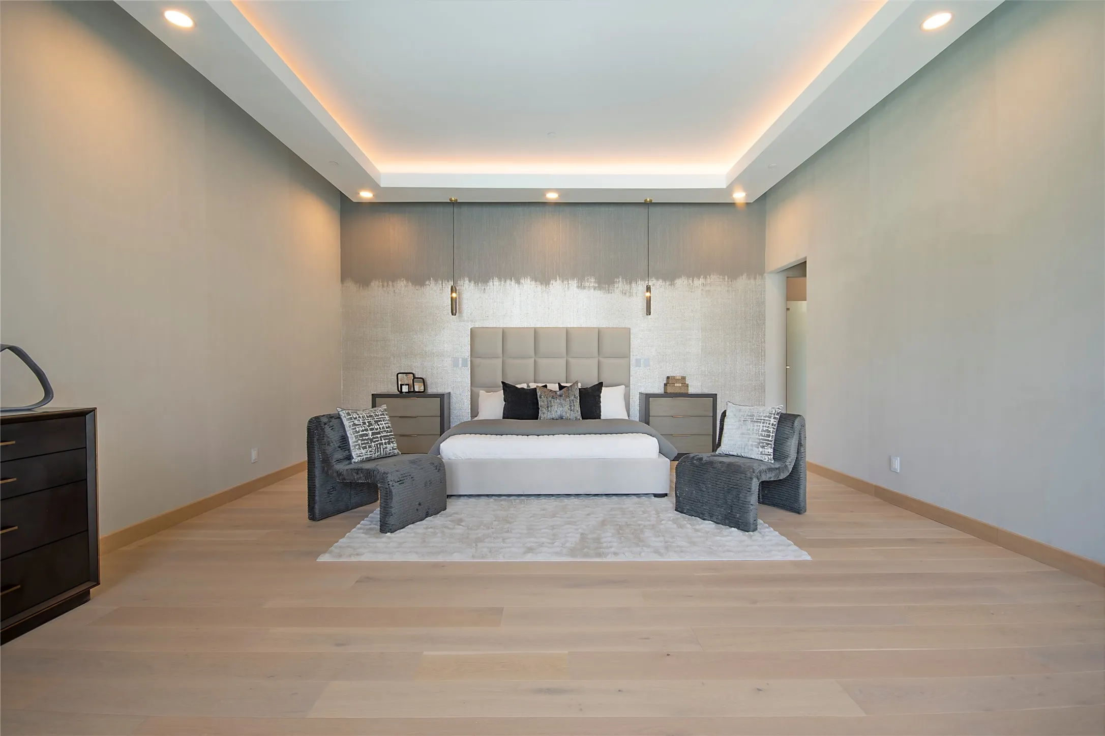 Tray ceiling with recessed lighting and cove lighting, wood-finish flooring, accent wall with textured finish, modern pendant lighting fixtures, and an open doorway