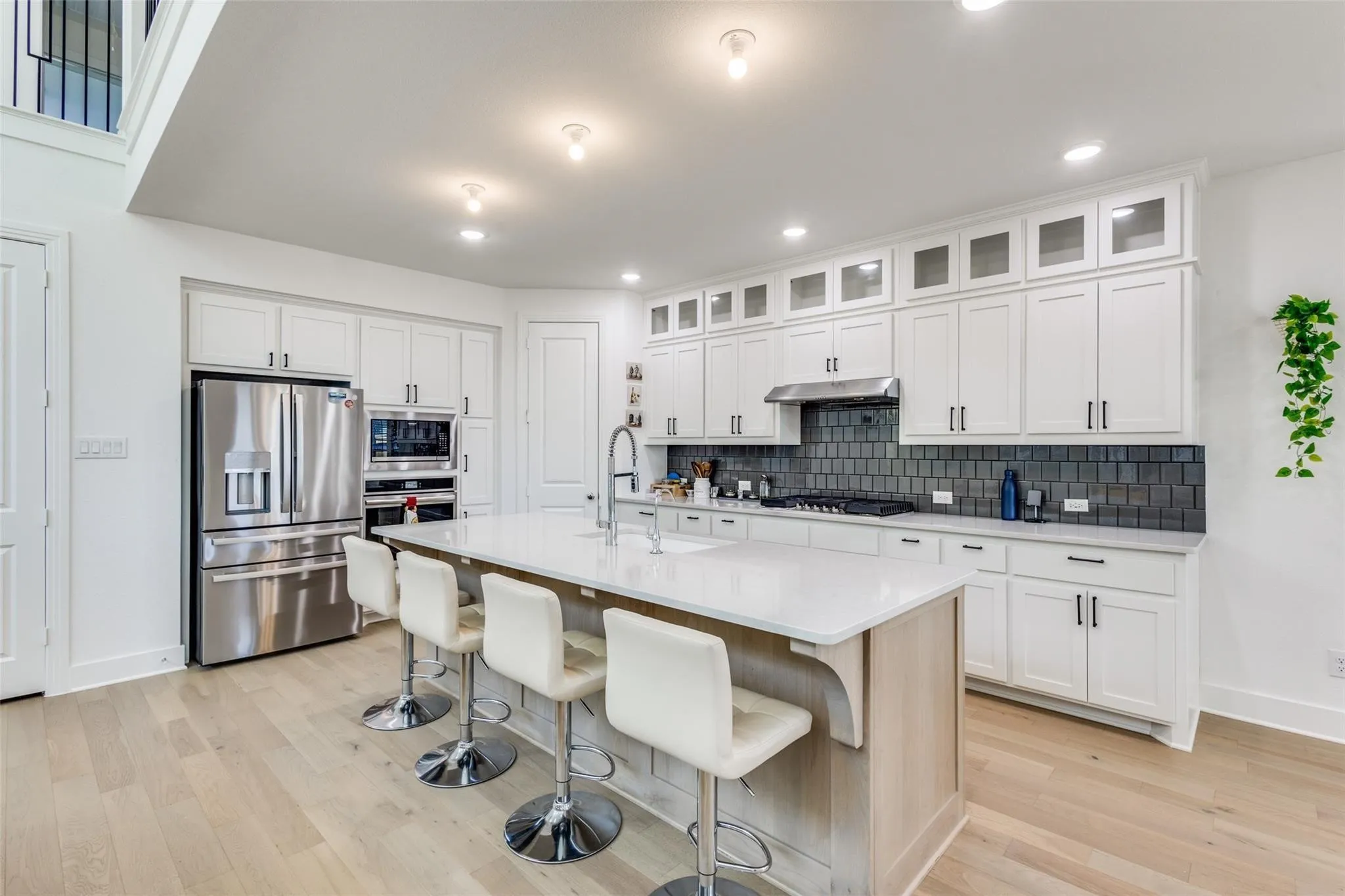 Contemporary kitchen featuring extensive white cabinetry, stainless steel appliances, a large center island with seating, and wood-finish flooring