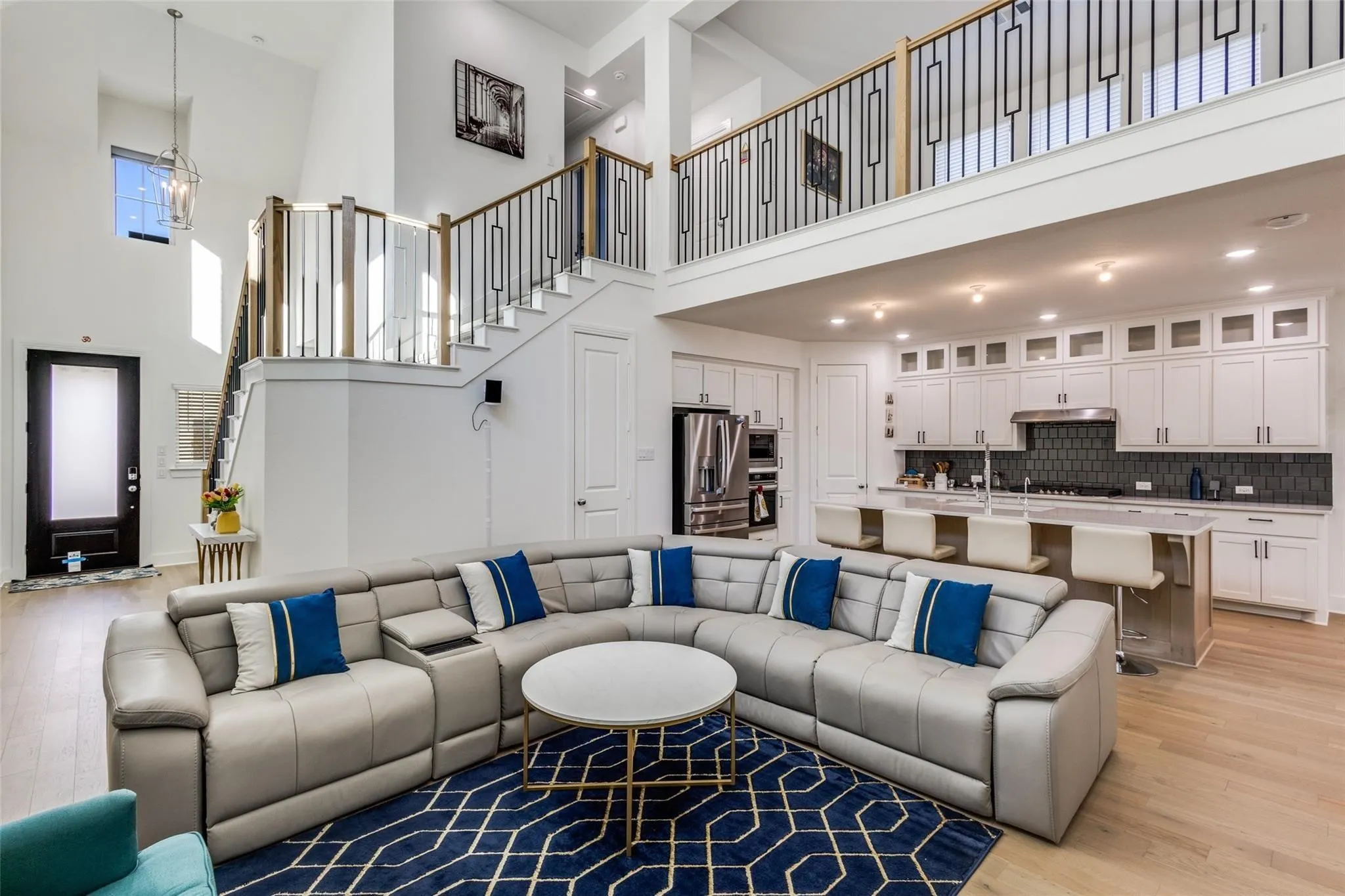Soaring ceilings with a decorative chandelier, open-concept kitchen with stainless steel appliances, breakfast bar seating, custom cabinetry, and a two-story staircase with modern railings
