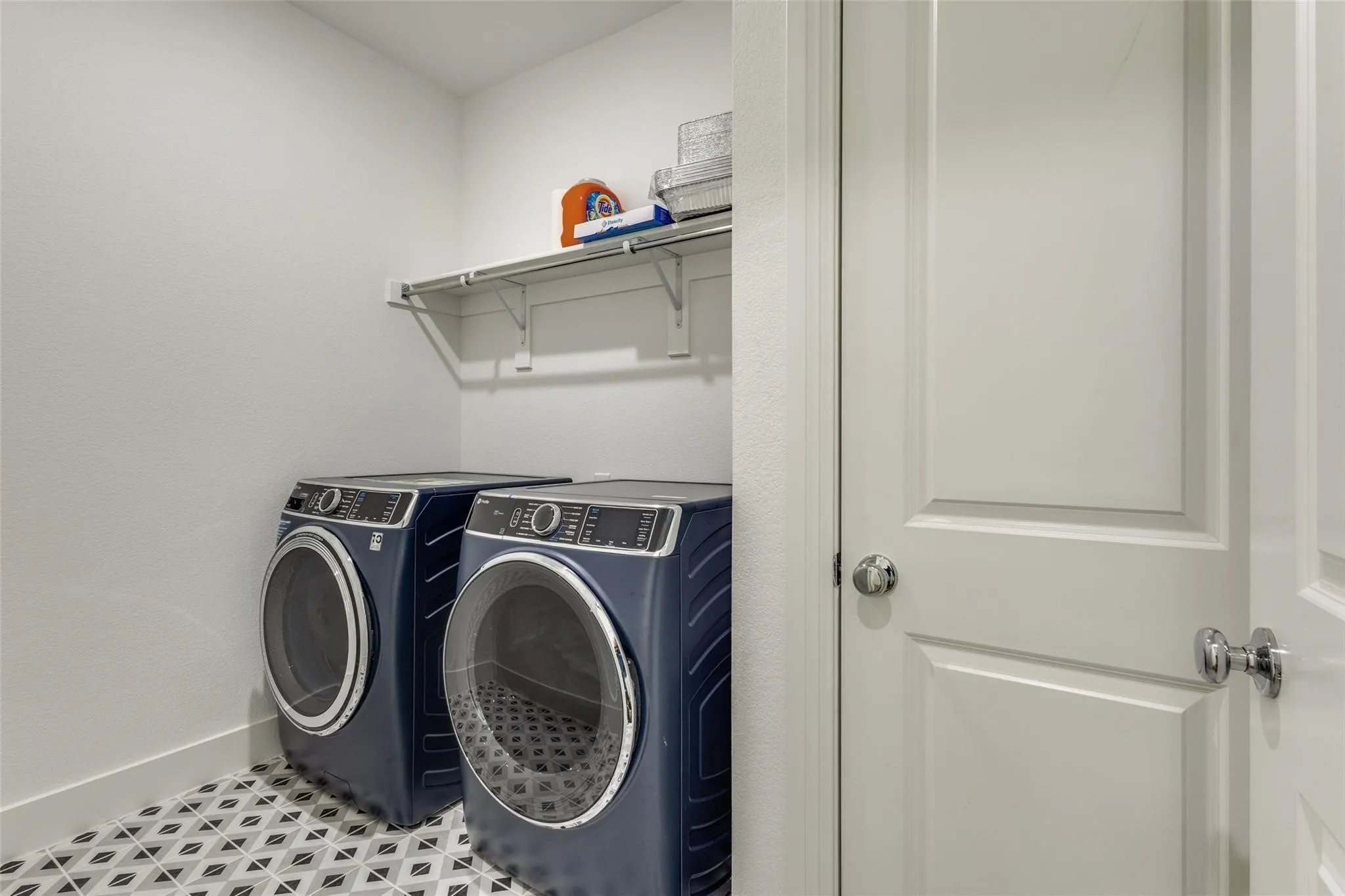 Laundry area featuring a patterned tile floor, built-in shelving, and a panel door with chrome hardware