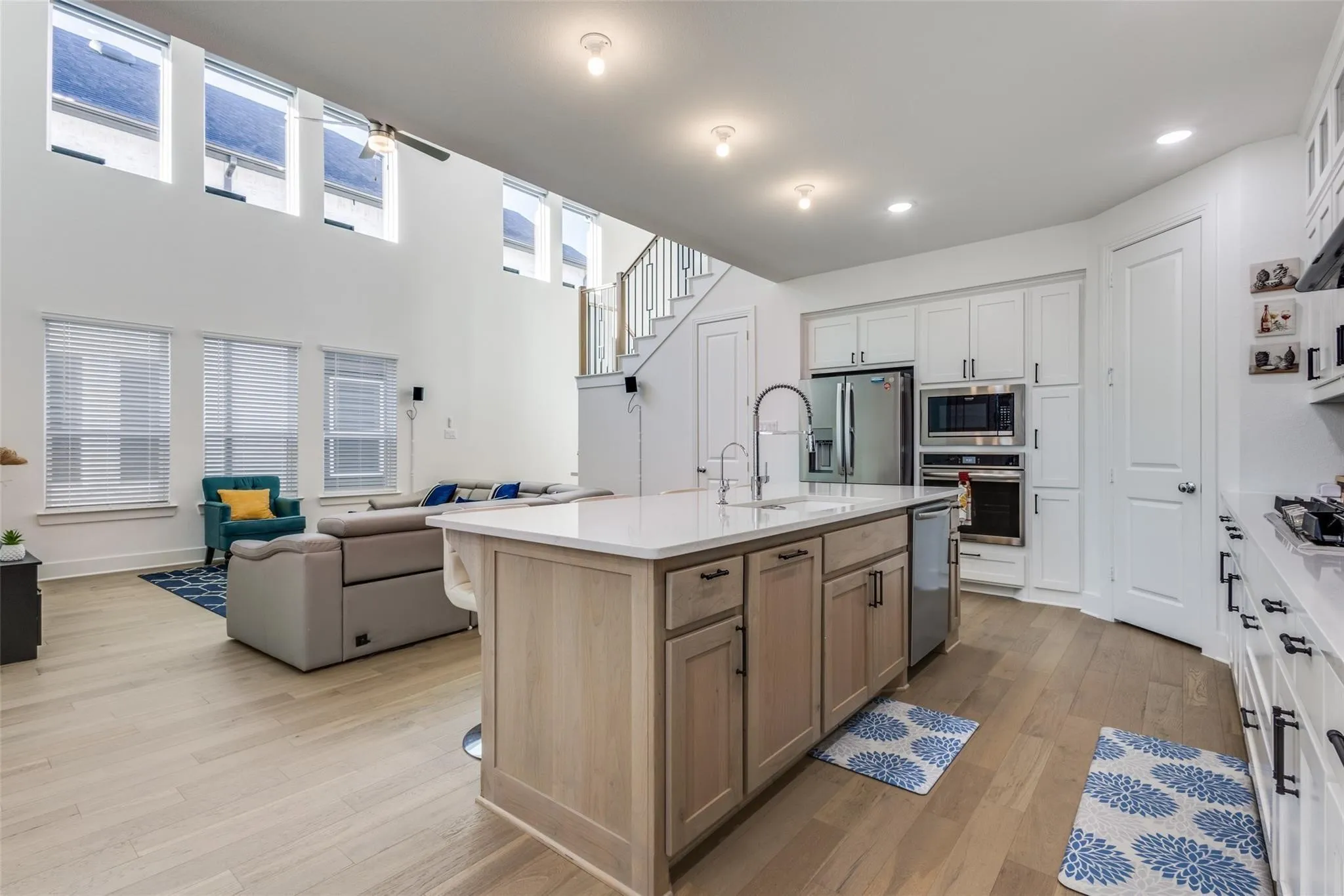 Open-concept kitchen with a large island, white cabinetry, built-in stainless steel appliances, and wood-finish flooring
