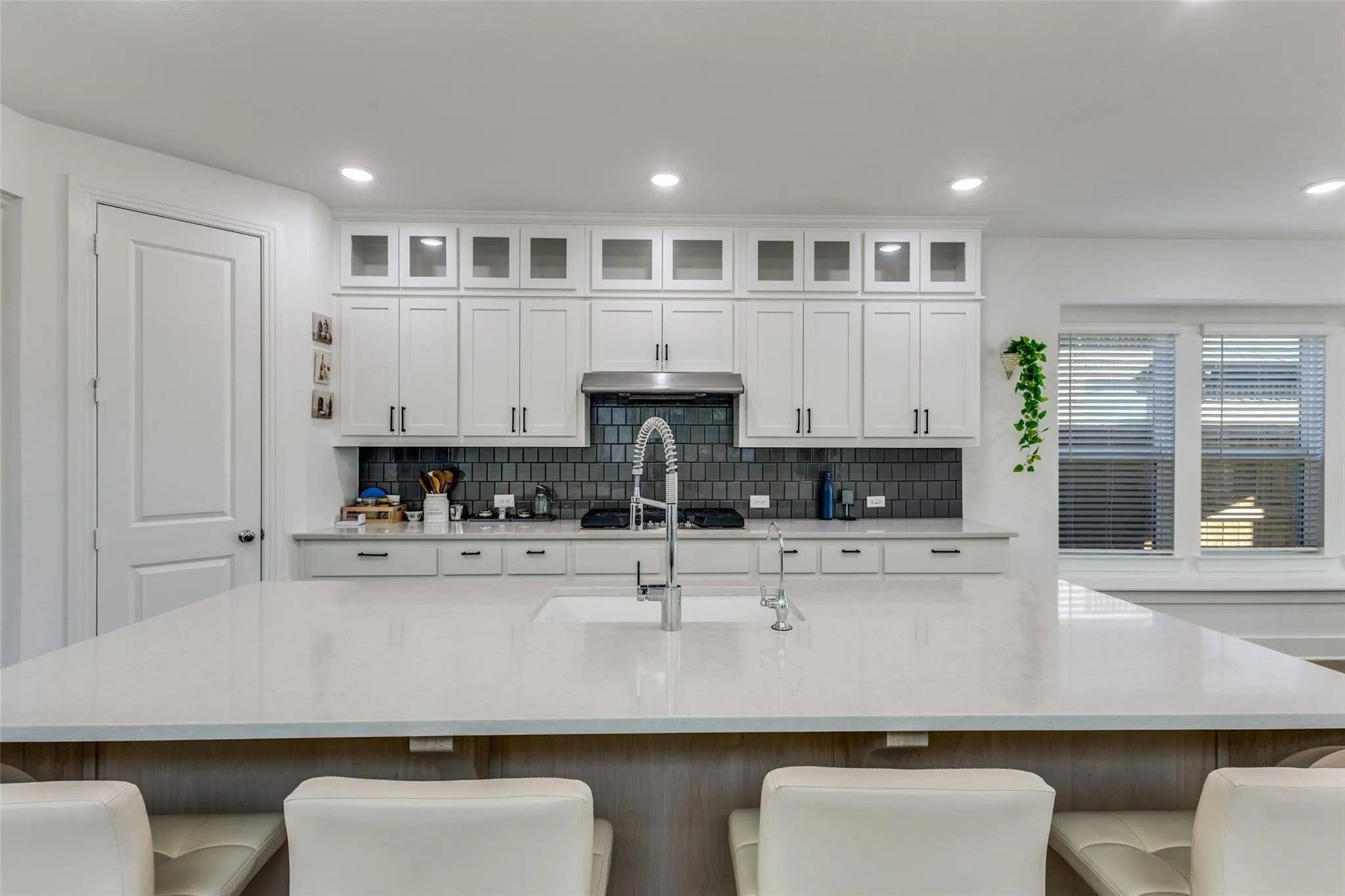 Spacious kitchen island with a built-in sink, white shaker cabinetry, dark subway tile backsplash, and stainless steel appliances