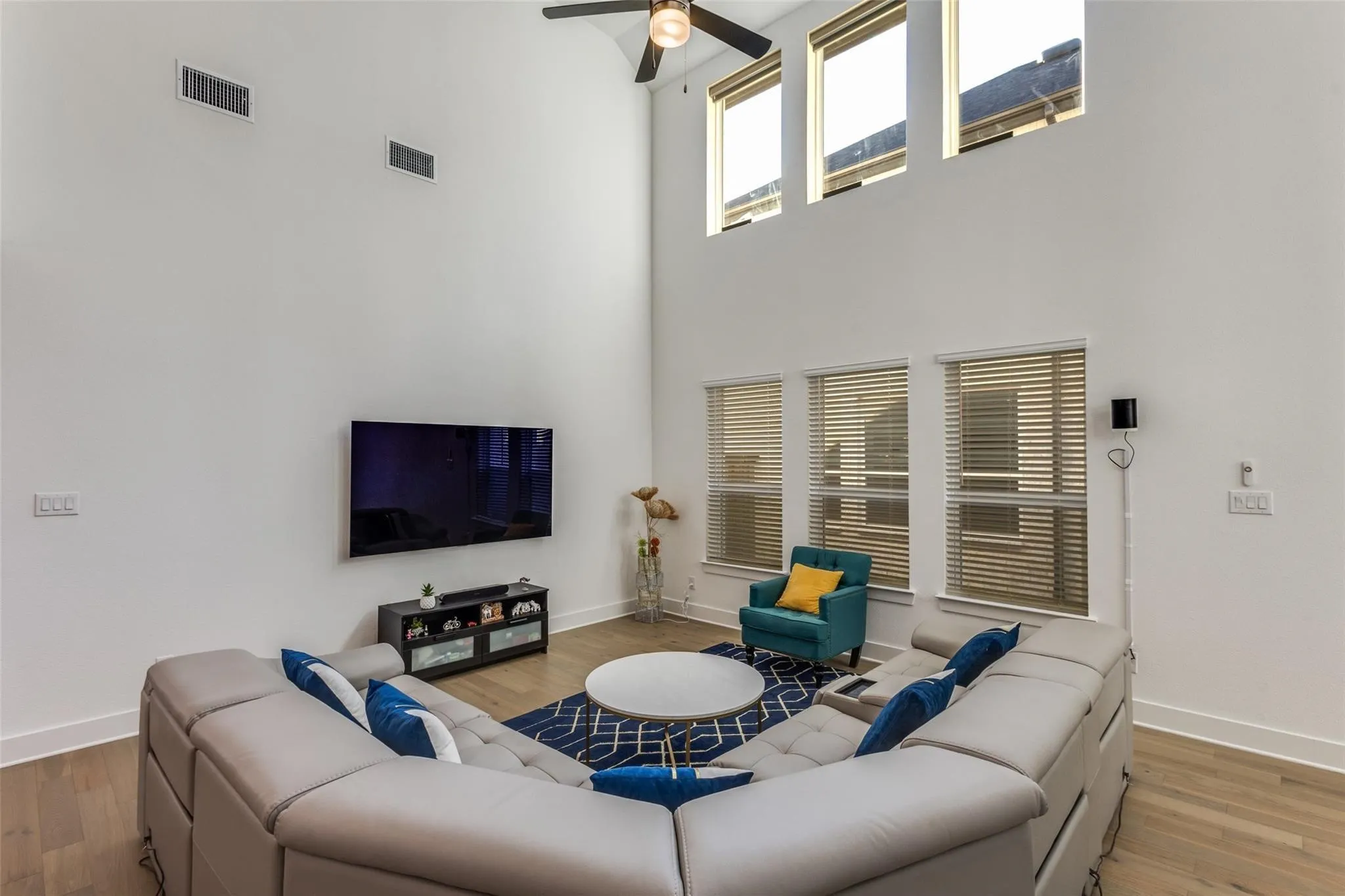 Double-height ceiling, wood-finish flooring, ceiling fan, and multiple windows with blinds