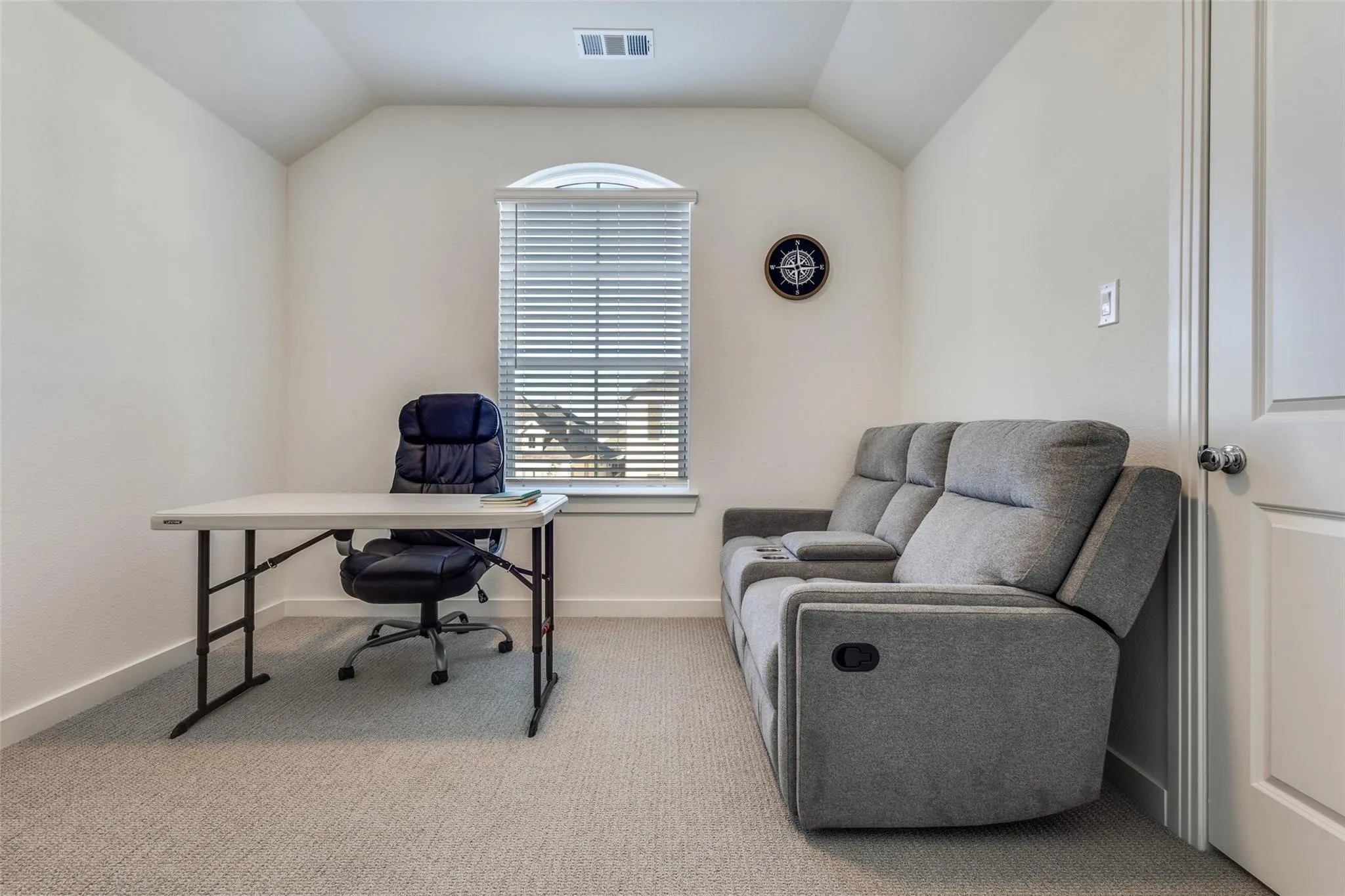 Carpeted room with a vaulted ceiling, a single arched window featuring blinds, and an interior door