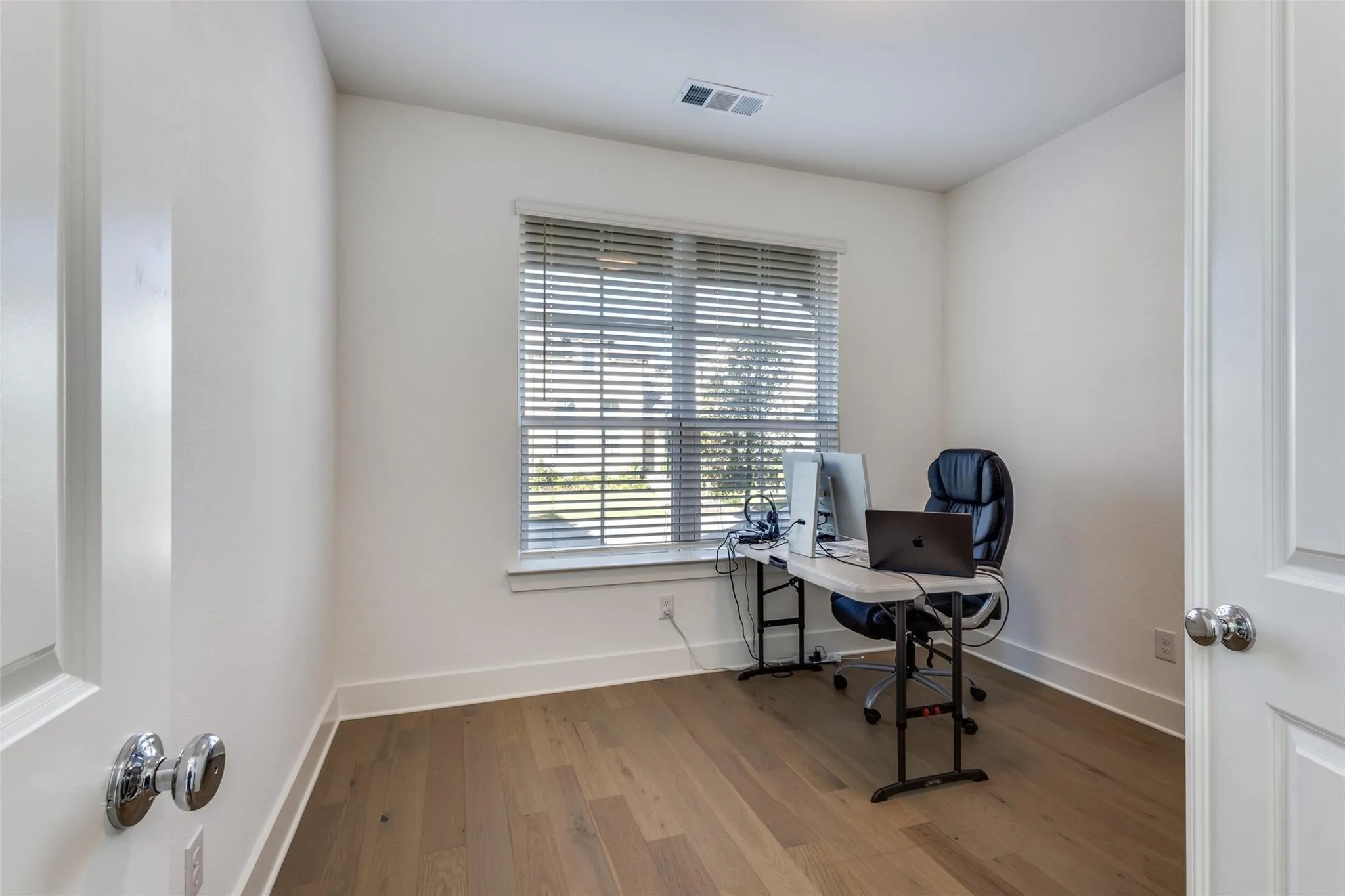 Wood-finish flooring, white walls, and a window with horizontal blinds