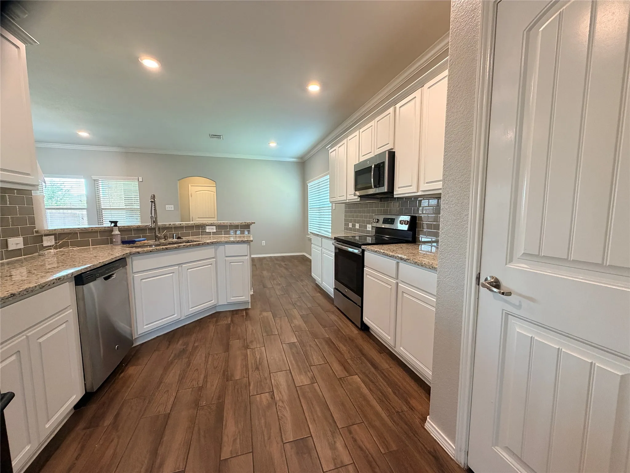 Kitchen featuring white cabinetry, granite countertops, a subway tile backsplash, stainless steel appliances, and wood-finish flooring