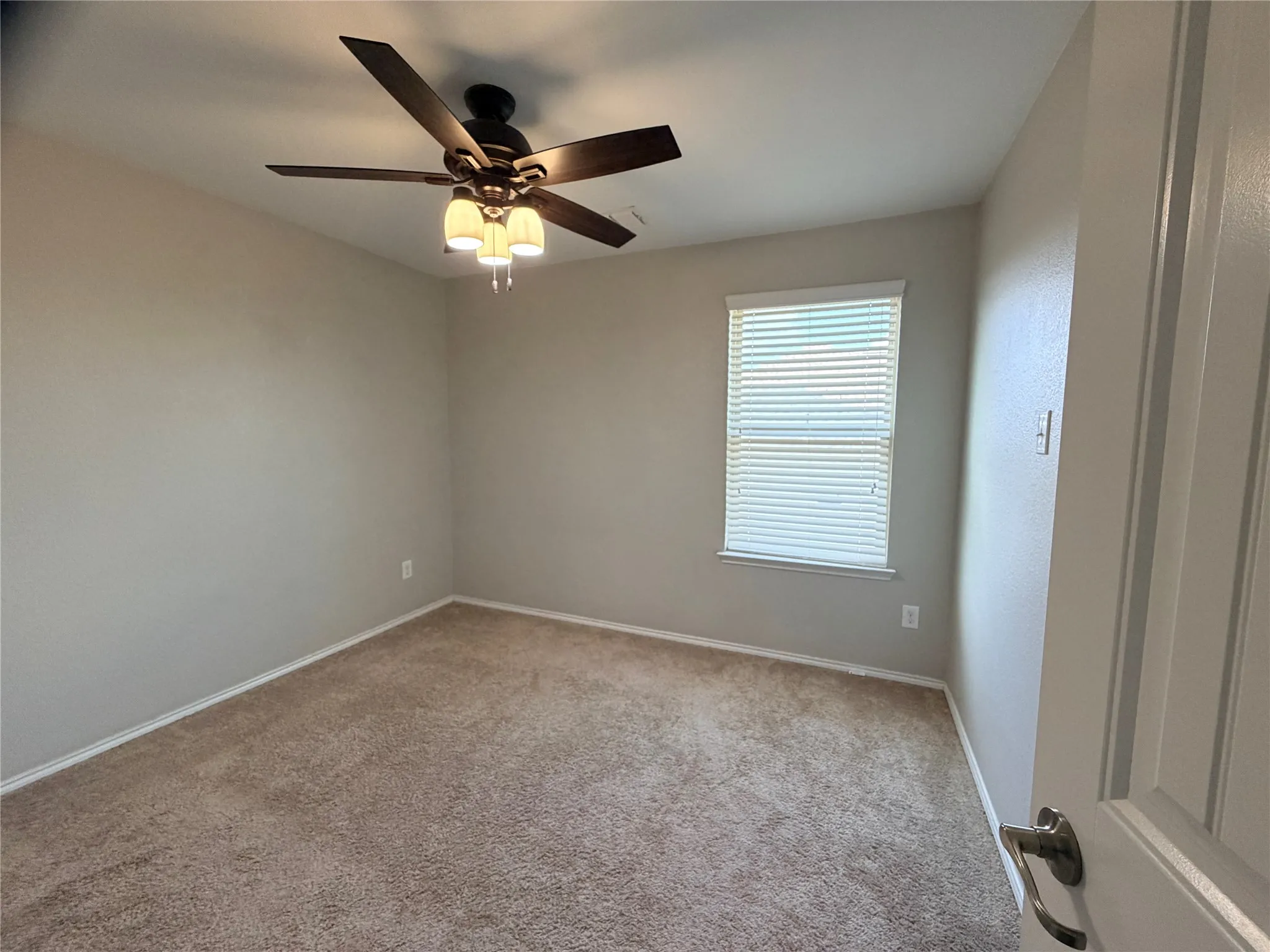 Neutral tone wall paint, textured carpeting, window with blinds, ceiling fan with integrated lighting