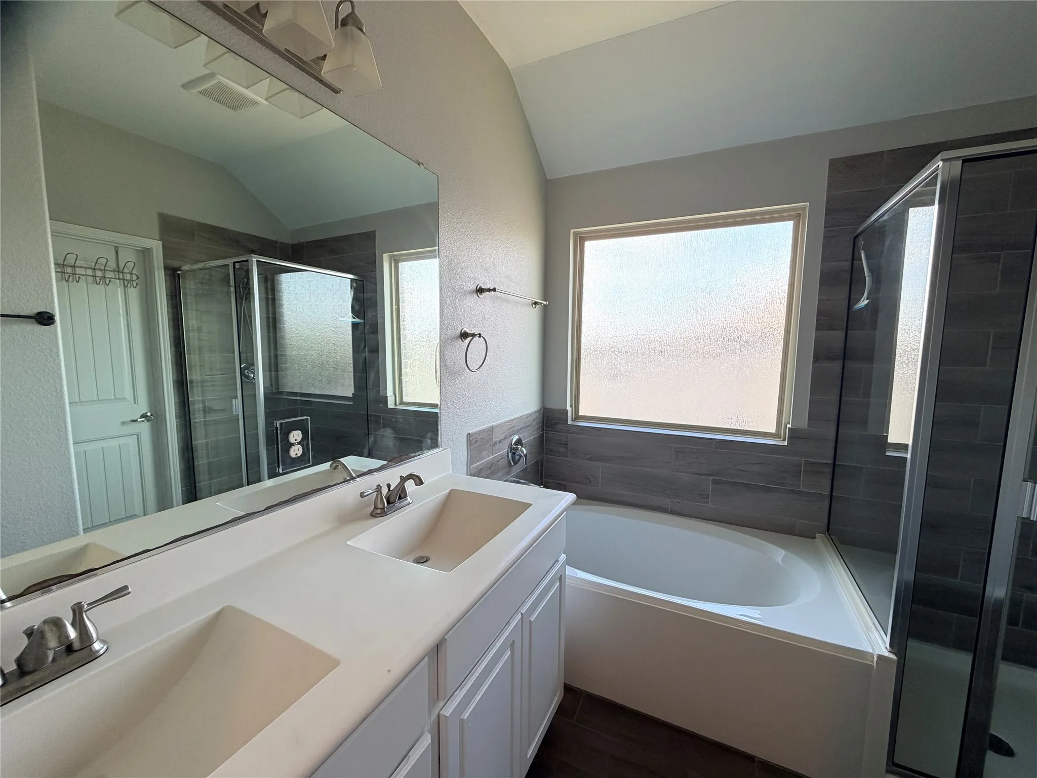 Double vanity with integrated sinks, full-width mirror, glass-enclosed shower, bathtub, and wood-finish flooring