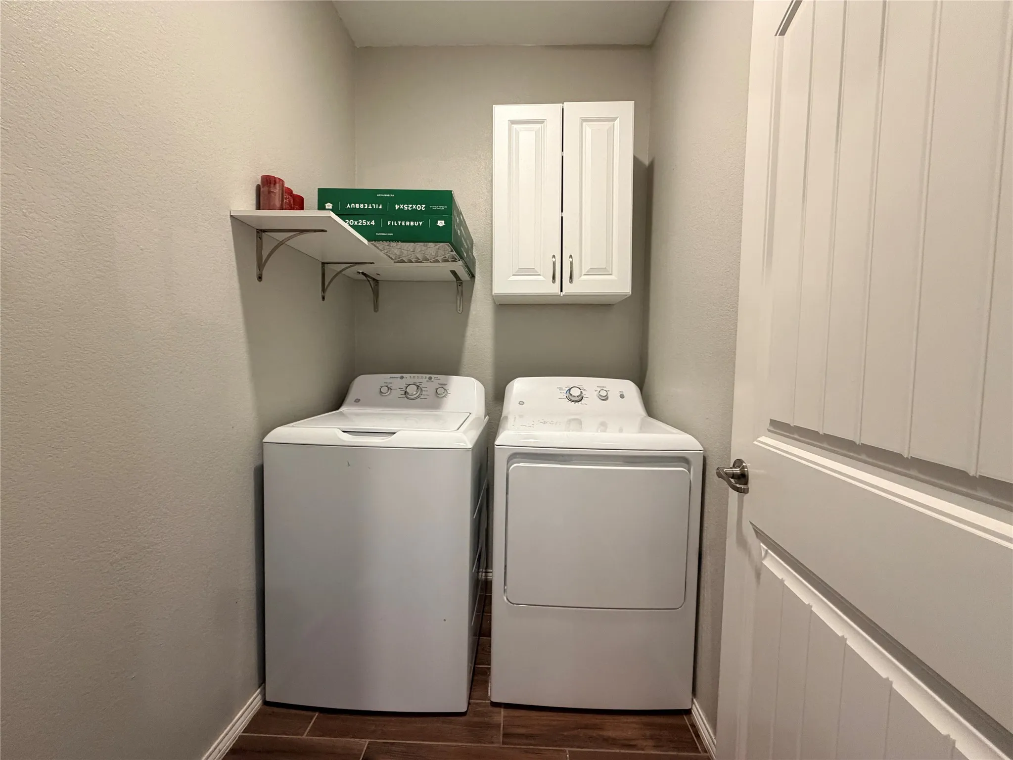 Laundry area featuring wood-finish flooring, white wall-mounted cabinetry, and corner shelving