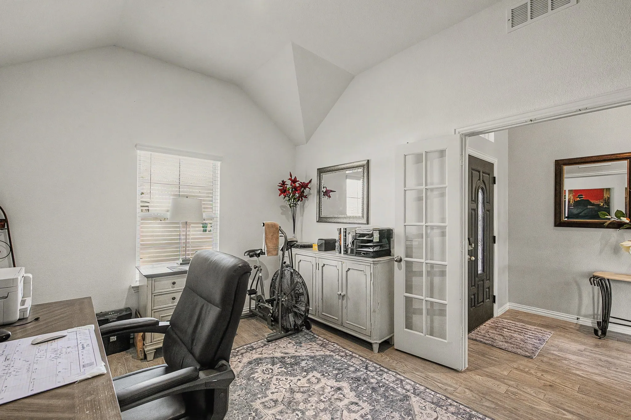 Vaulted ceiling, wood-finish flooring, white window blinds, white French doors, and a decorative front door