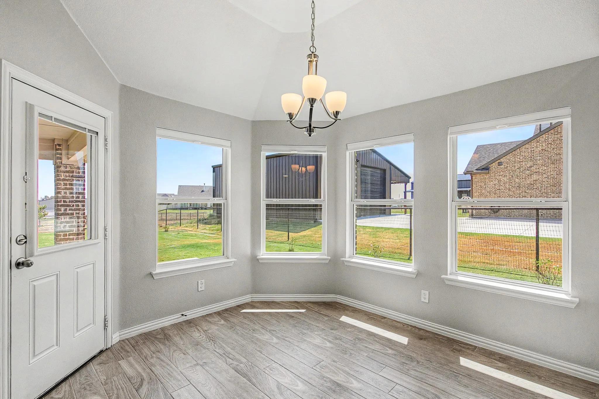 Vaulted ceiling with a chandelier, wood-finish flooring, multiple windows, and a glass-paneled door