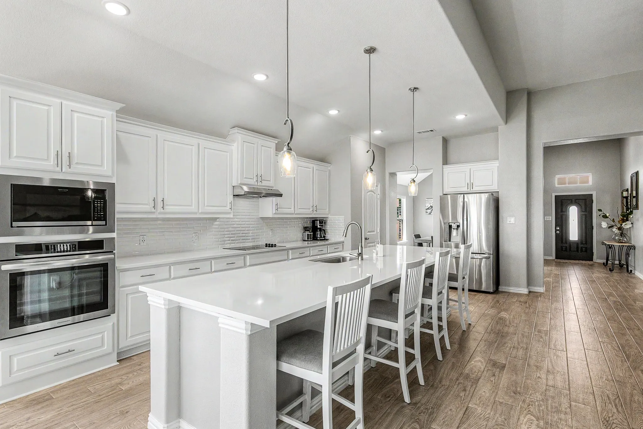 Kitchen featuring a large central island with seating, stainless steel appliances, white cabinetry, recessed lighting, and wood-finish flooring