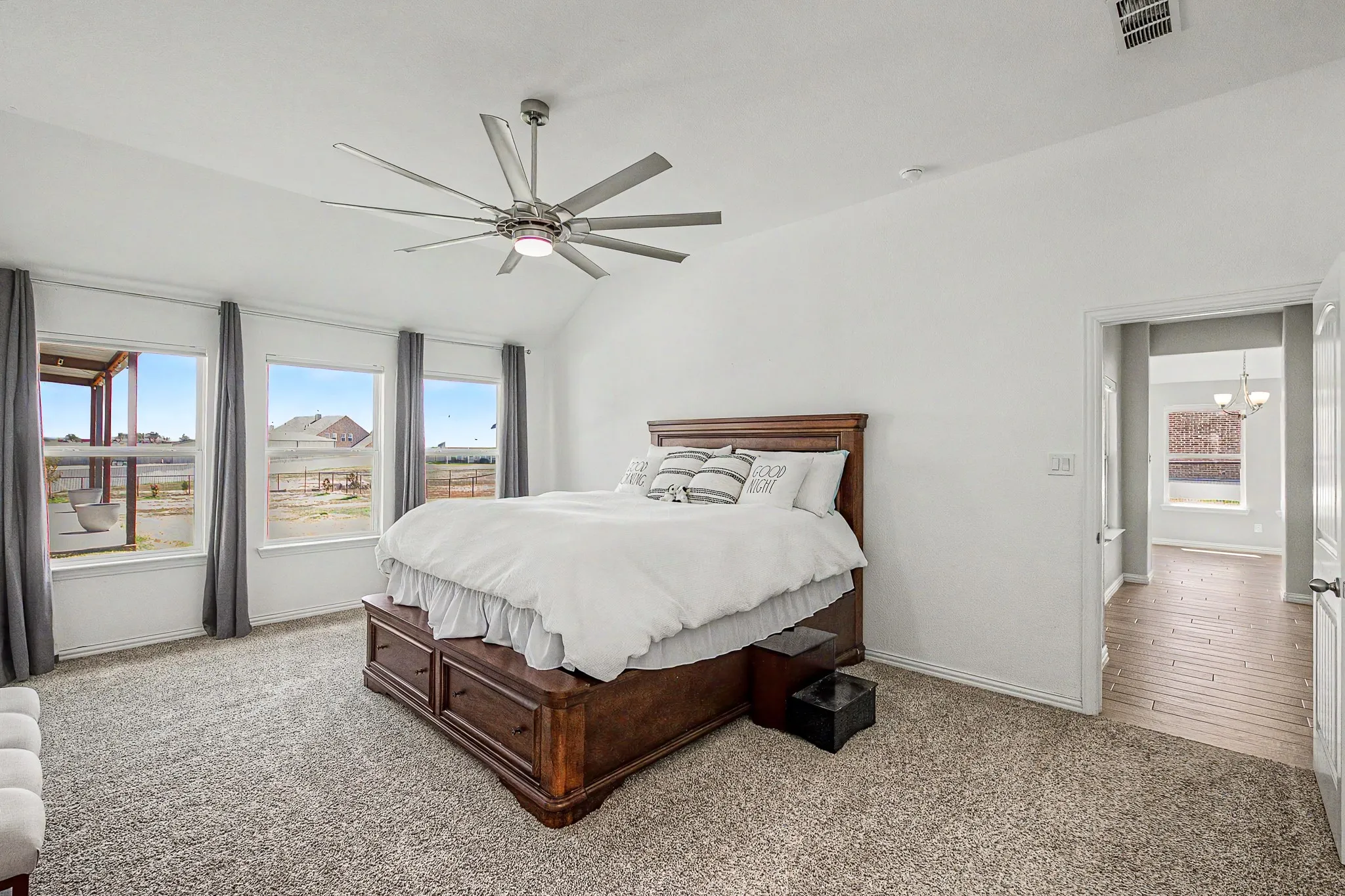 Vaulted ceiling with a contemporary ceiling fan, multiple windows, carpeted flooring, and a doorway opening to a room with wood-finish flooring