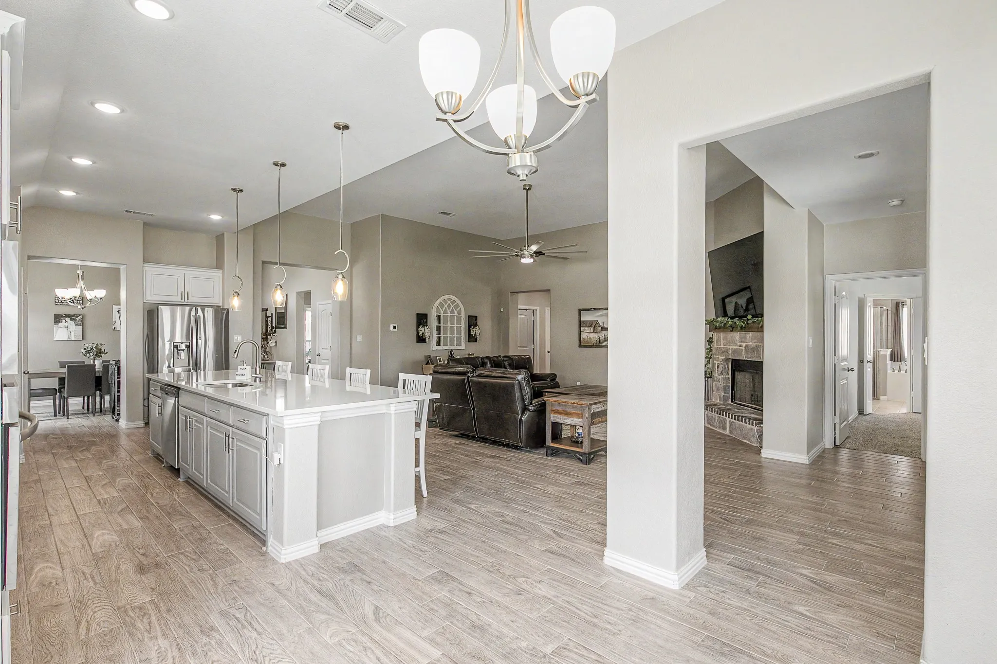 Open-concept living space featuring wood-finish flooring, a kitchen island with seating, stainless steel appliances, a stone fireplace, and recessed lighting