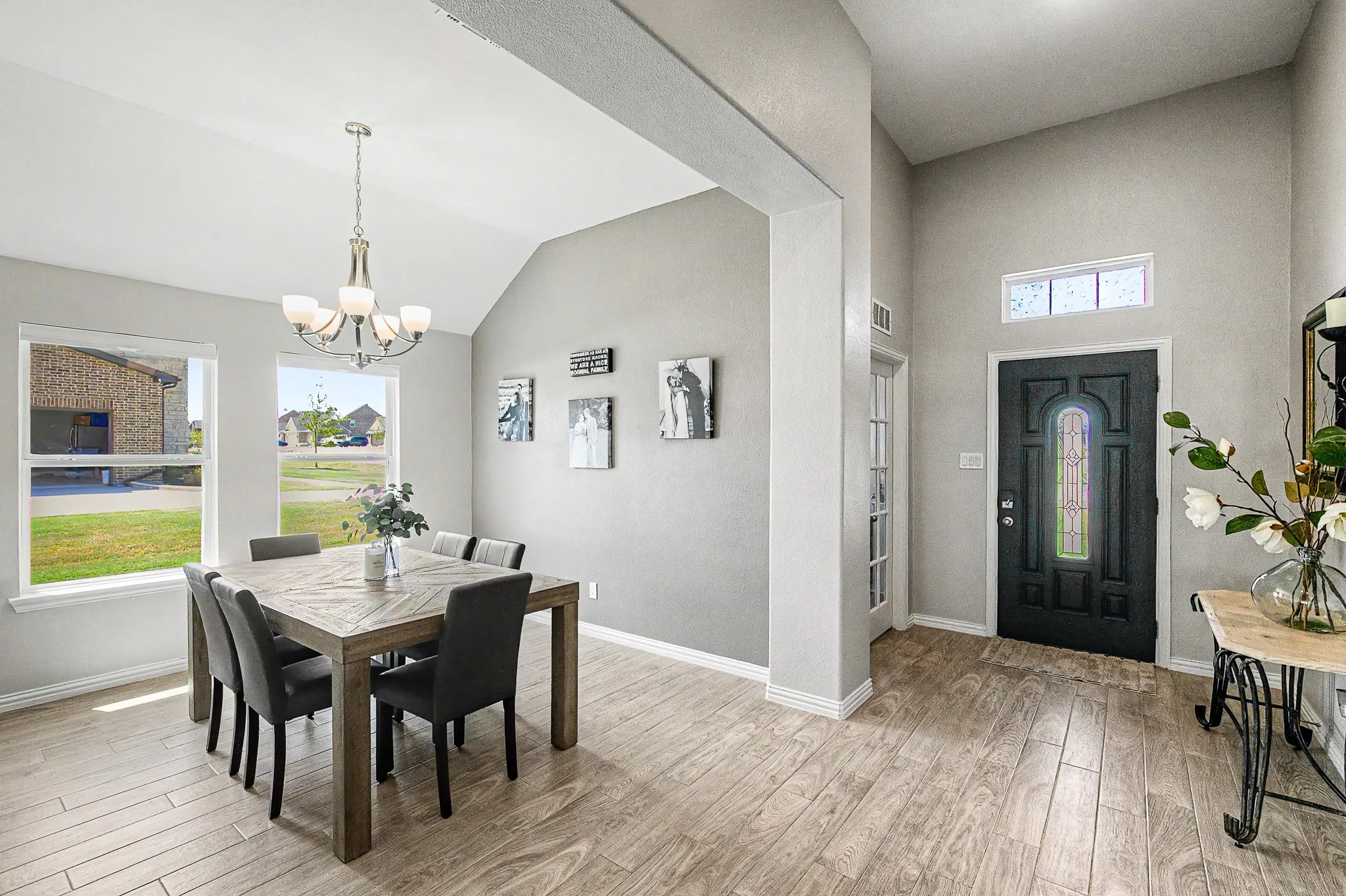 Vaulted ceiling with chandelier lighting, wood-finish flooring, and a decorative front door with transom window